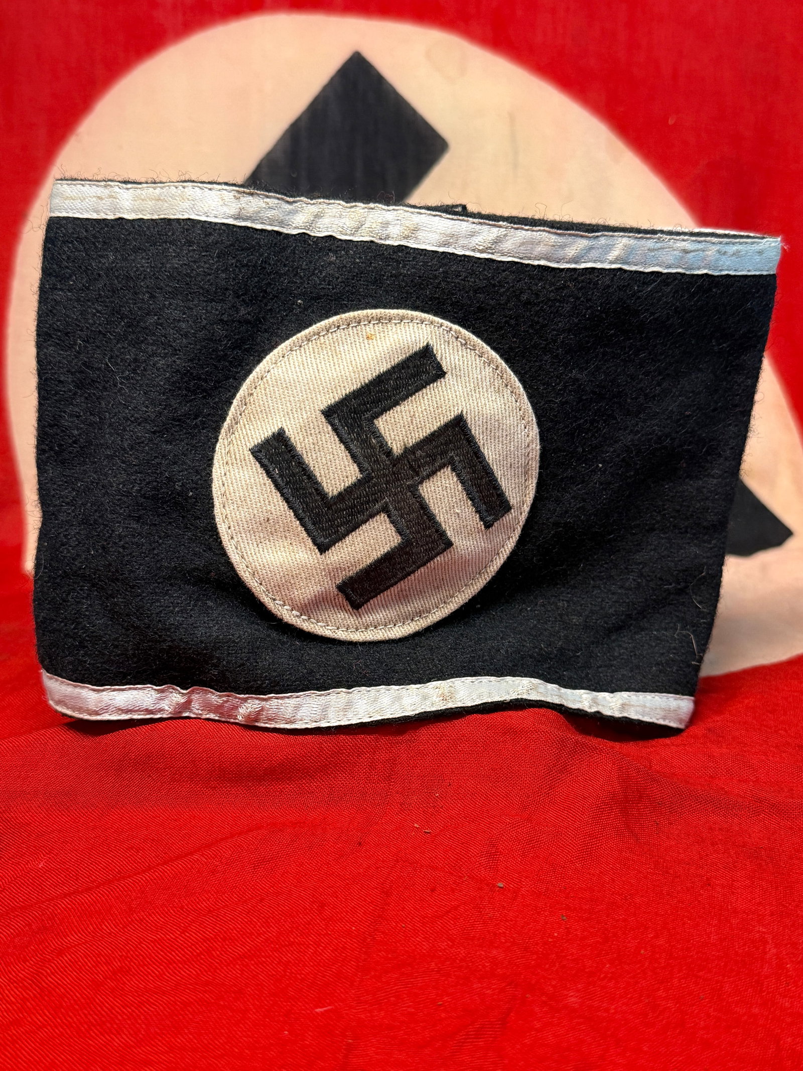 WWII German NSDAP Black Swastika Armband with Silver-Gray Borders – RZM Labeled: A distinctive black wool armband centered by a separately applied light-colored circular field bearing a prominently embroidered black swastika. Narrow silver-gray woven borders run along both the upp