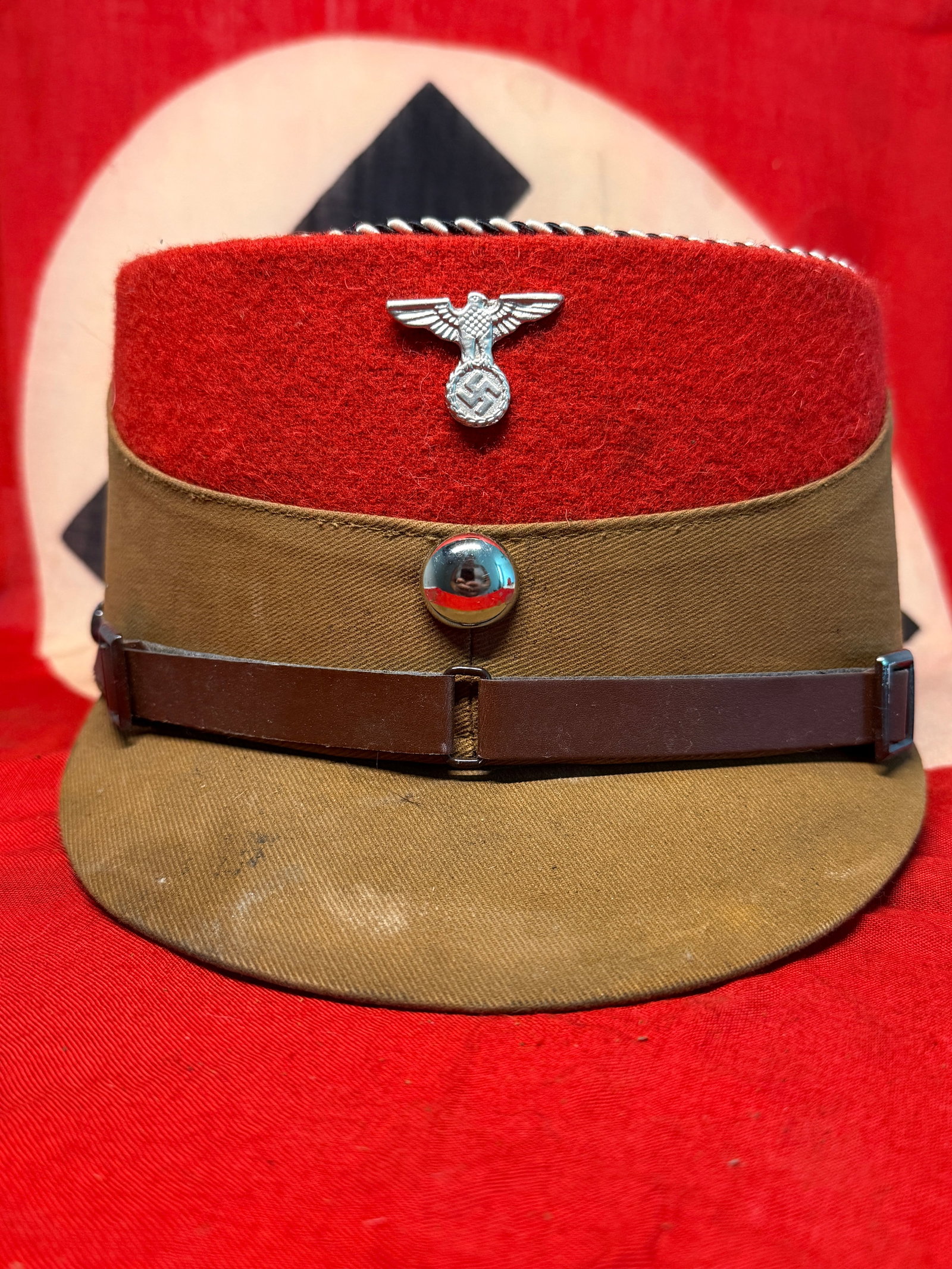 WWII German SA Brown & Red Kepi with Eagle & Swastika Insignia – RZM Labeled: An imposing WWII-era German political uniform kepi constructed with a brown/tan body, broad red wool crown section, matching cloth-covered visor, and contrasting brown leather chinstrap secured by met