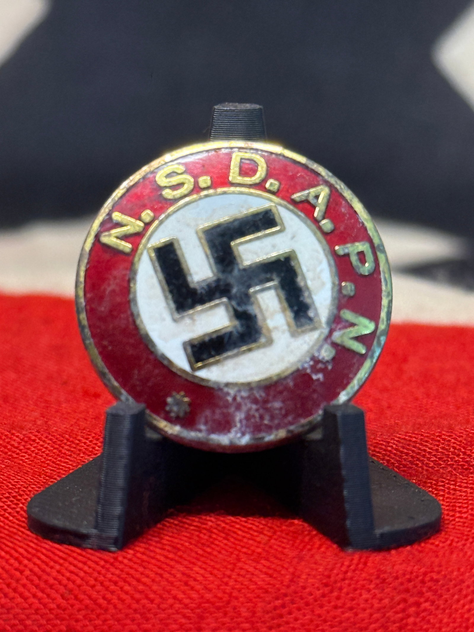 Third Reich WW2 German NSDAP Enamel Membership Badge – M1/129 Marked: A circular red, white, black, and gold-colored NSDAP membership badge displaying a central black swastika against a white enamel field, surrounded by a red enamel border carrying the raised gold lette