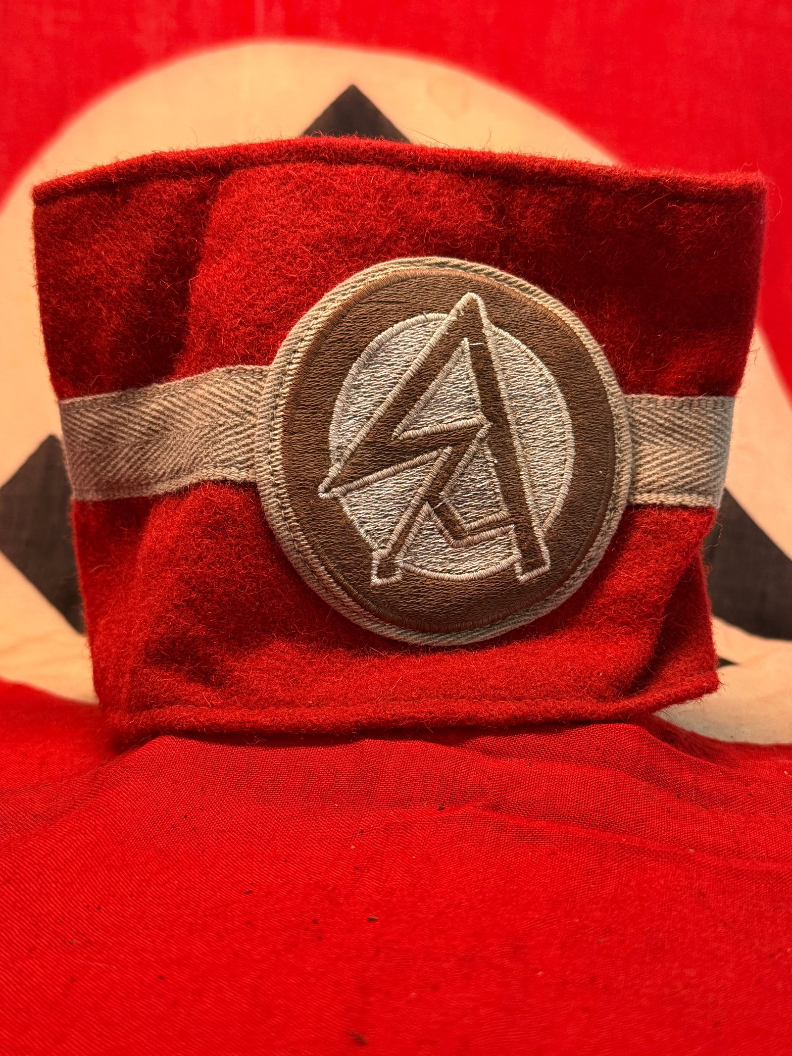 Third Reich German SA Sturmabteilung Red Wool Armband with RZM Label: A striking red wool armband associated with the SA (Sturmabteilung), distinguished by a large circular embroidered insignia featuring the organization’s interlocking “SA” monogram. The centr