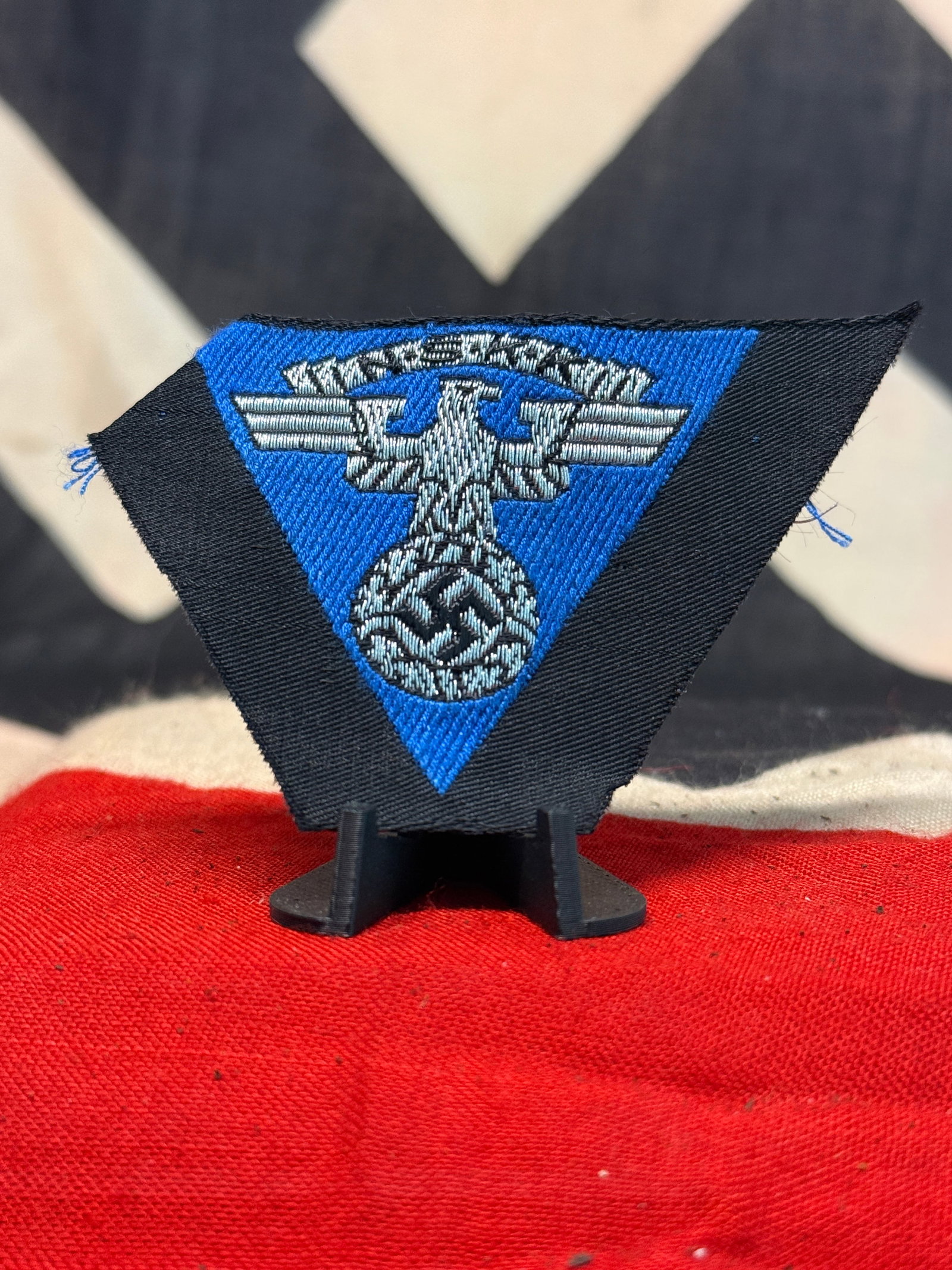 WWII German NSKK National Socialist Motor Corps Overseas Cap Triangle Eagle Insignia: A distinctive WWII German NSKK (Nationalsozialistisches Kraftfahrkorps / National Socialist Motor Corps) overseas-cap insignia, constructed on a downward-pointing blue textile triangle with black surr