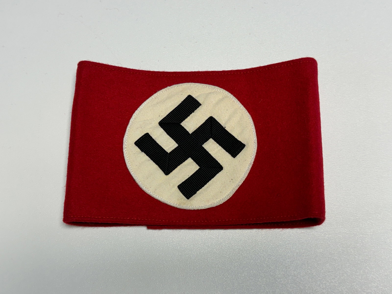 WWII German NSDAP Party Swastika Wool Armband: WWII German NSDAP political armband constructed from red wool fabric with a large circular white cloth field applied to the front and a prominent black swastika formed from separately applied ribbed t