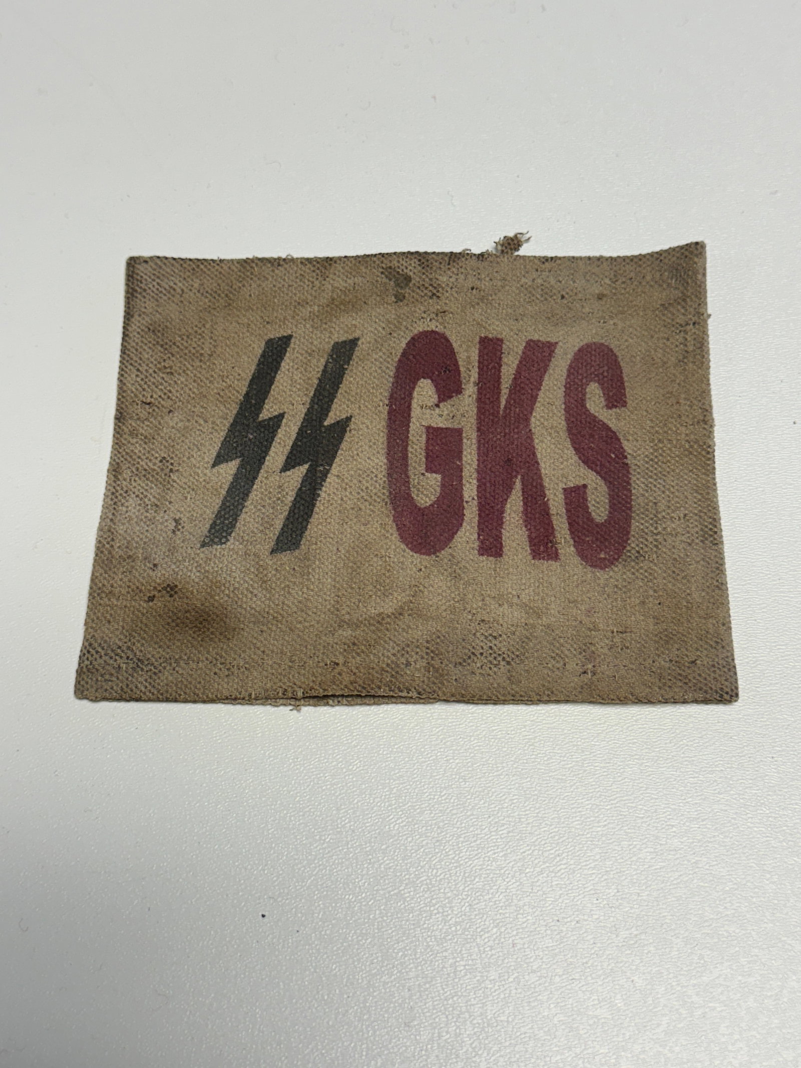 WWII German Waffen-SS GKS Printed Cloth Identification Armband: WWII German Waffen-SS associated cloth identification armband or sleeve band constructed from coarse tan woven fabric and prominently printed with black SS runes alongside large burgundy-red “GKS&rd