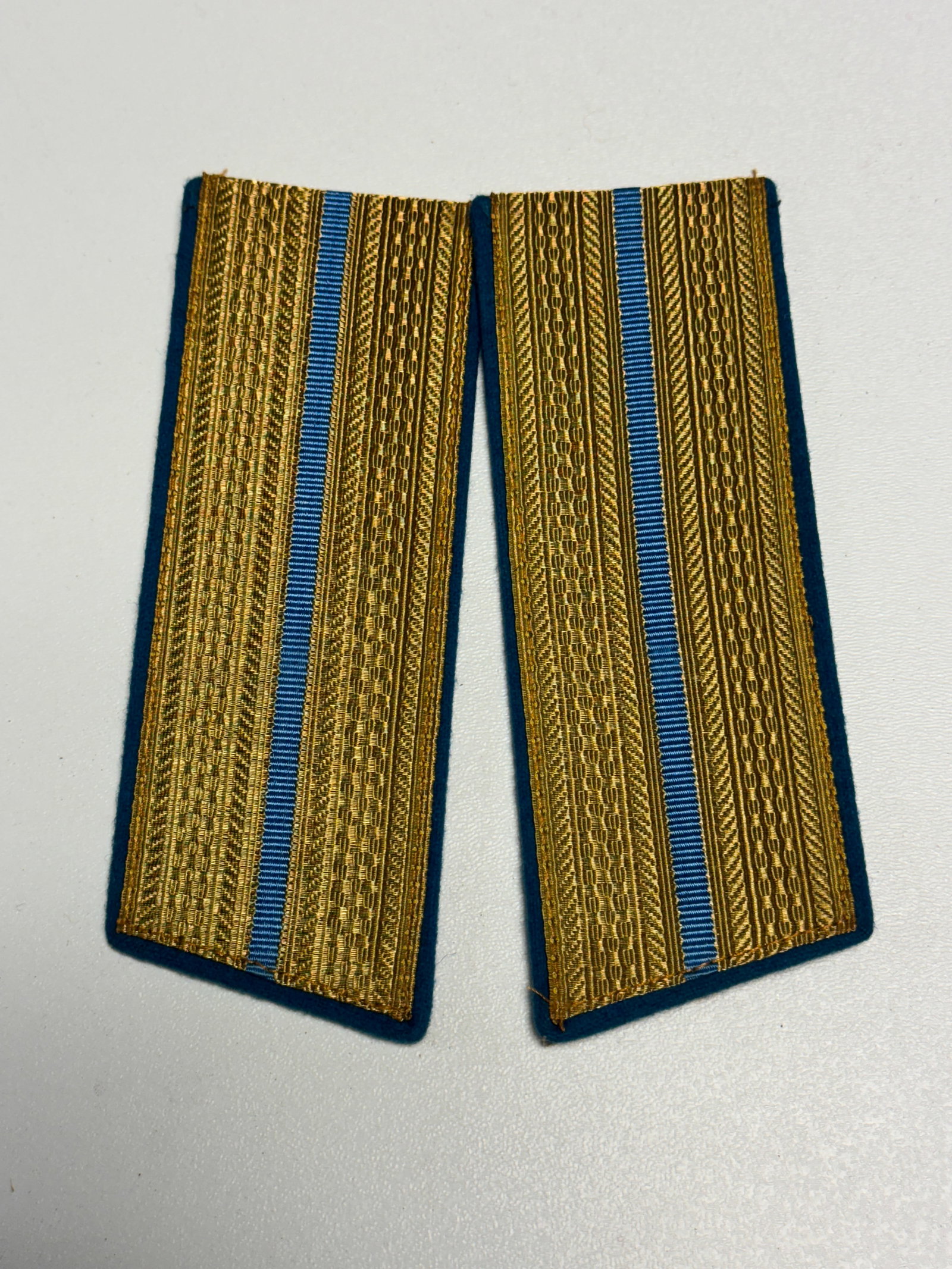 WWII German Luftwaffe Officer Gold Bullion Shoulder Boards – Blue Branch Pair: WWII German Luftwaffe officer shoulder board pair featuring richly woven gold-colored metallic bullion construction over a deep blue wool backing, each displaying a narrow blue central stripe running 