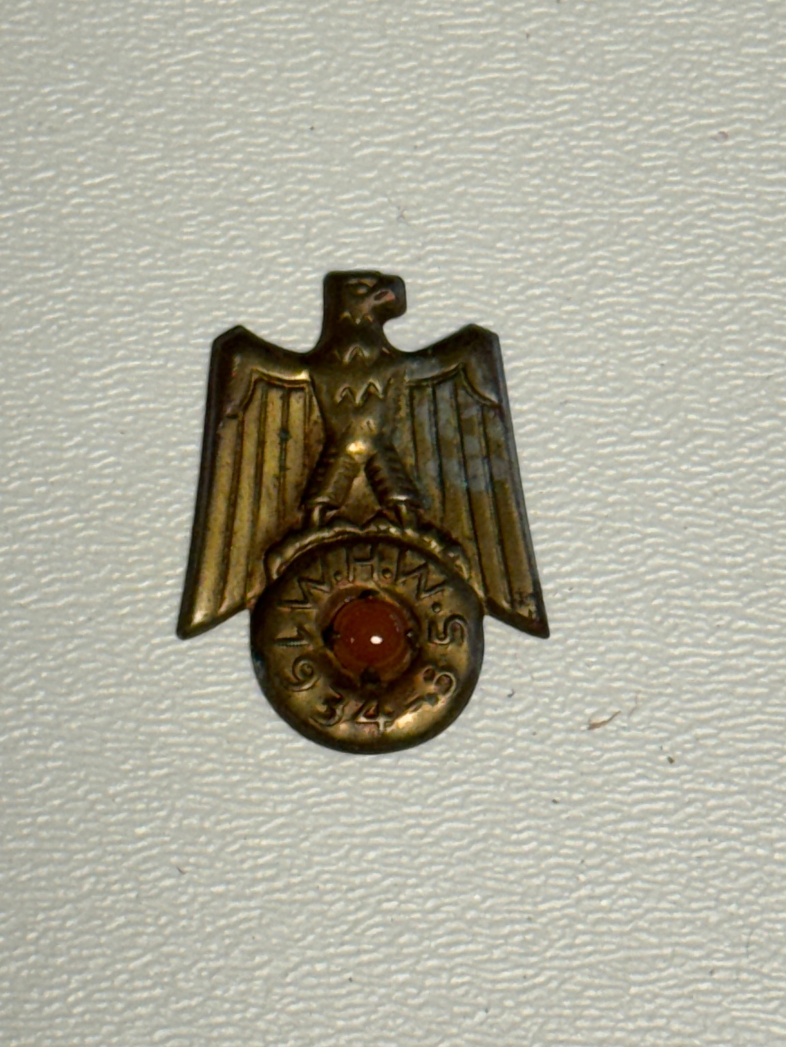 WWII German NSDAP Political Eagle Membership Badge with Red Center: WWII German political organization badge featuring a spread-wing eagle above a circular lower medallion bearing a red center and raised surrounding lettering that appears to read “NSDAP,” with