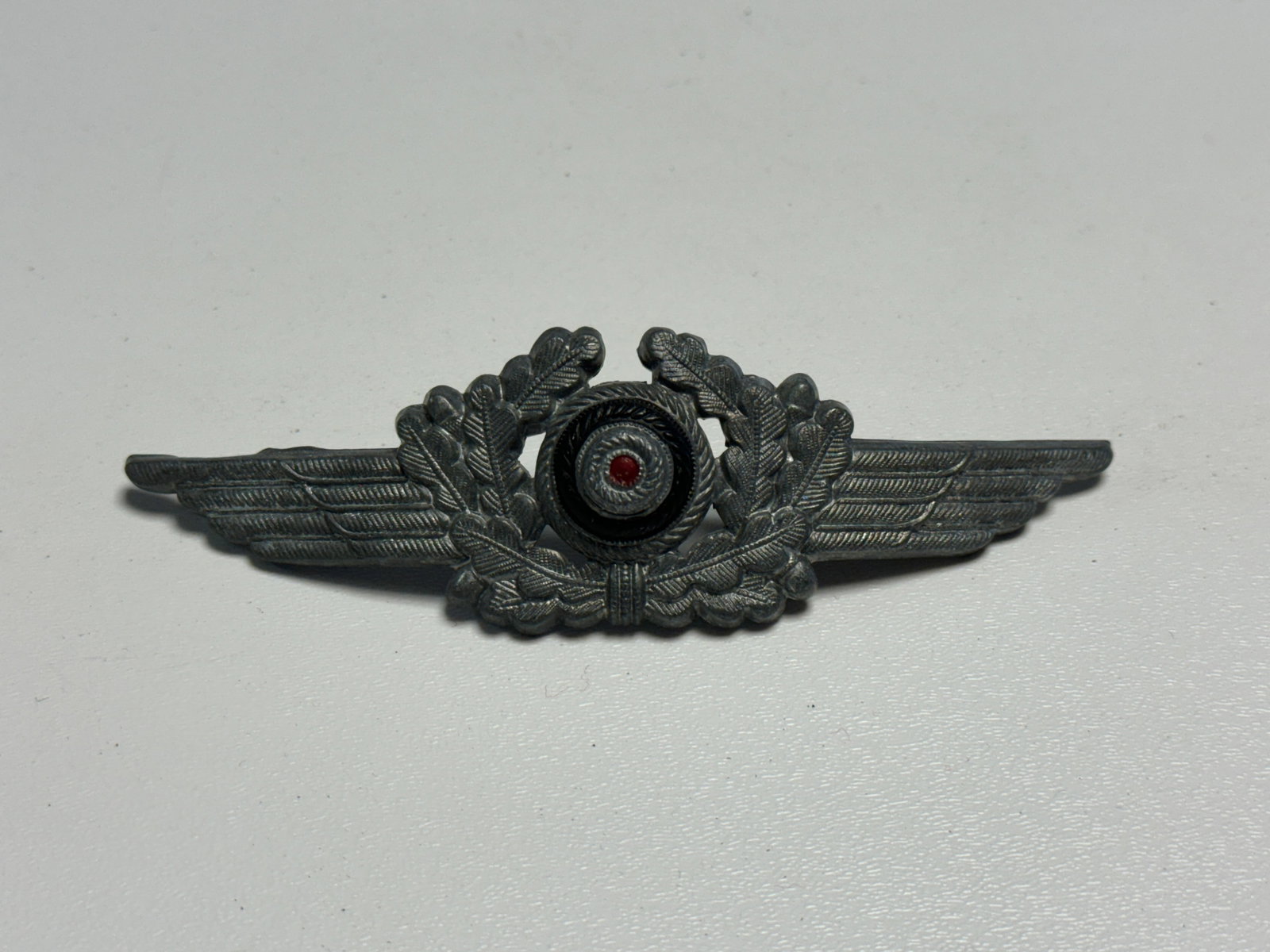WWII German Luftwaffe Officer Visor Cap Wreath & Winged Cockade Insignia: WWII German Luftwaffe officer visor cap insignia featuring an elaborate winged configuration with finely detailed feathering extending to either side of a central oak-leaf wreath. The center incorpora