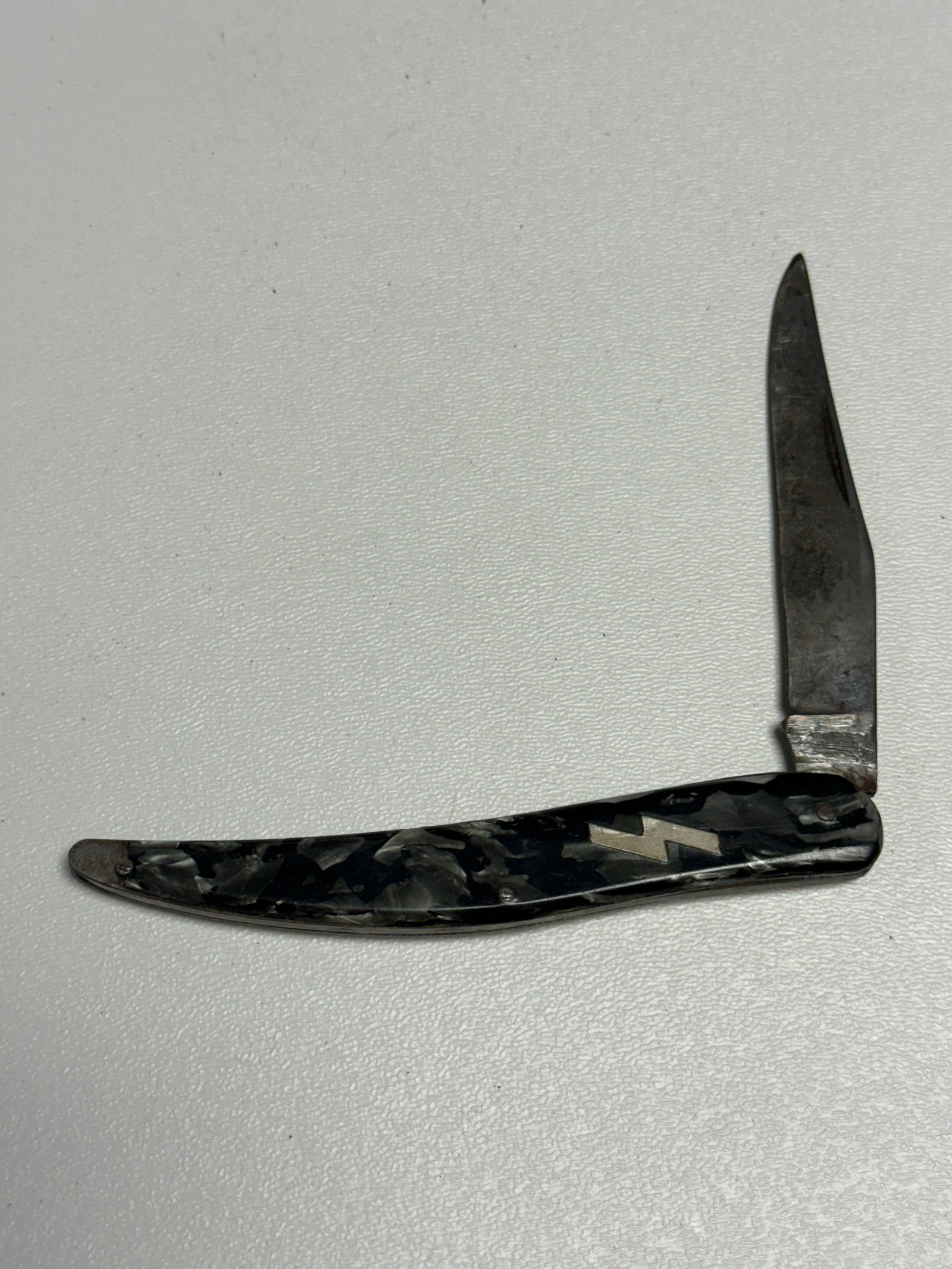 WWII German SS Lightning Bolt Inlaid Hitler Youth Folding Pocket Knife: WWII German Hitler Youth folding pocket knife featuring a slender curved handle fitted with black and gray marbled grip scales and an inset metal SS double lightning-bolt emblem. The knife is construc