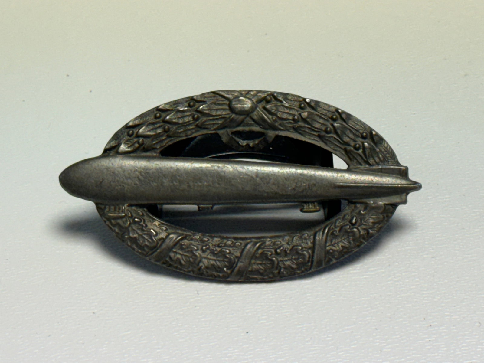 WWII German Kriegsmarine U-Boat Combat Badge – Submarine & Wreath Pin: WWII German Kriegsmarine U-Boat combat badge featuring an elongated submarine rendered horizontally across the center of an oval wreath, with finely detailed raised foliage and decorative relief throu