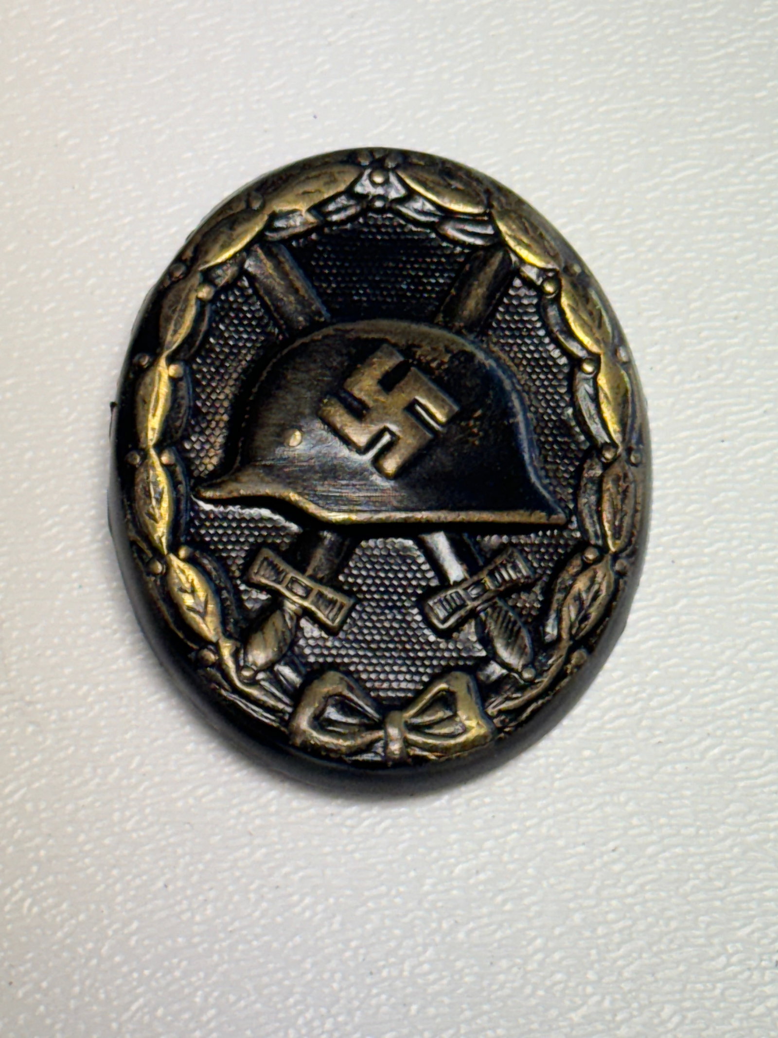 WWII German Army Heer Wound Badge in Black – Stahlhelm & Crossed Swords: WWII German Army Heer Wound Badge featuring the classic vertically oval design with a central German Stahlhelm bearing a raised swastika above crossed swords, all enclosed within a detailed laurel wre