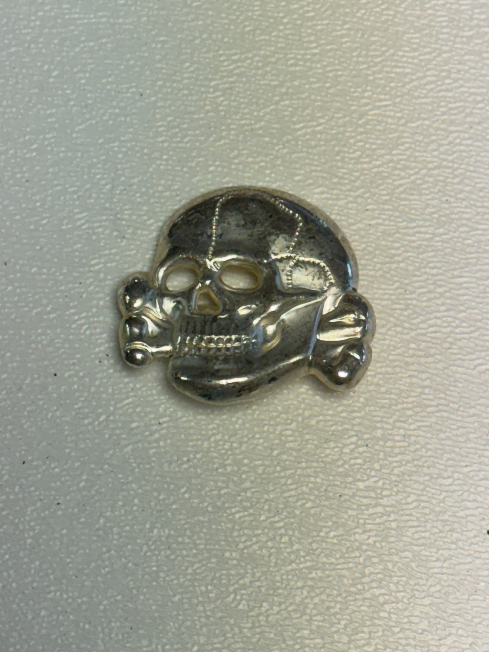 WWII German SS Totenkopf Skull Insignia – M1/52 RZM Marked: WWII German SS Totenkopf skull insignia featuring the distinctive frontal skull and crossbones design associated with SS headgear insignia of the Third Reich period. The piece is executed in a silver-