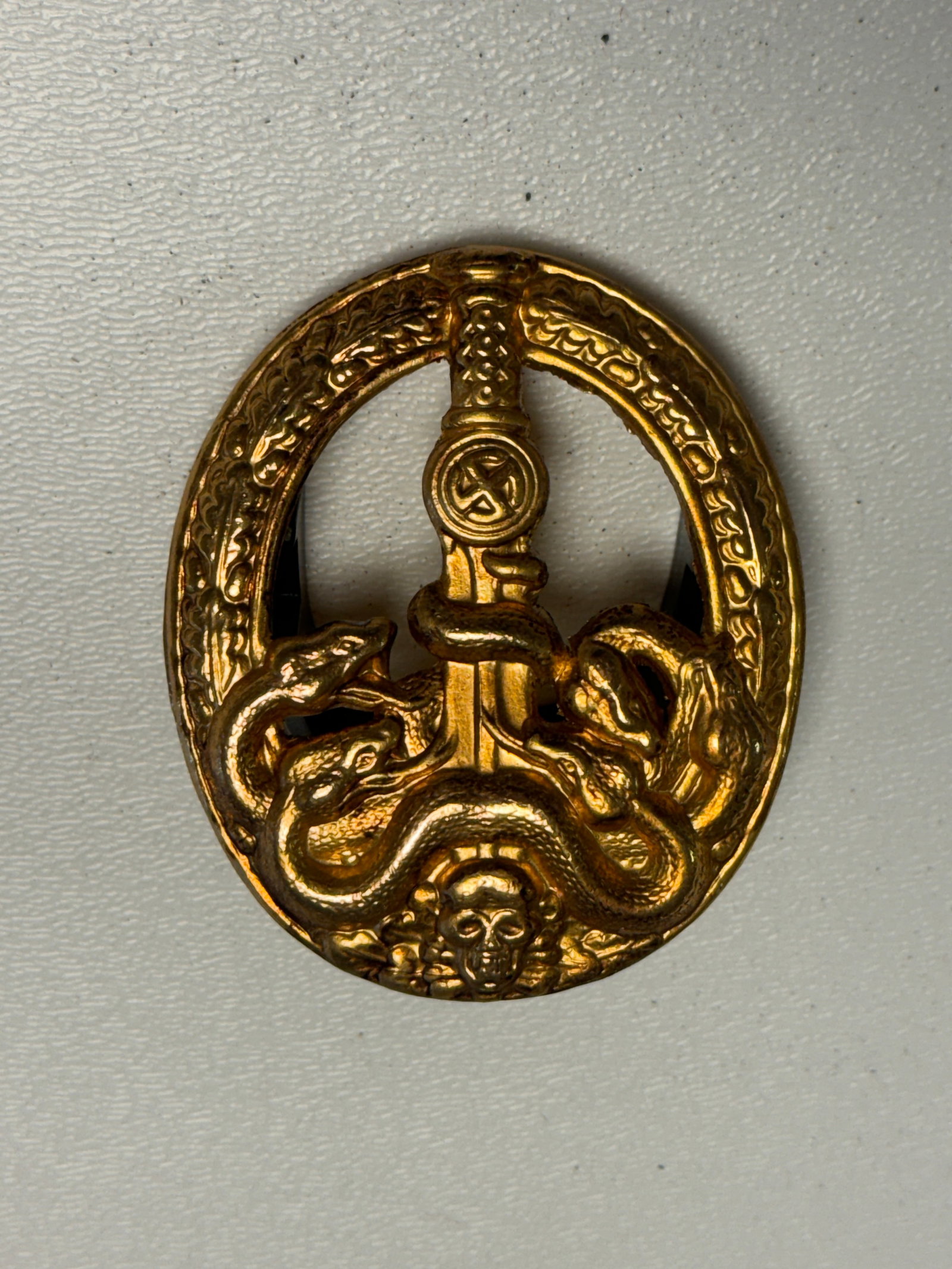 WWII German Anti-Partisan Badge in Gold – Sword & Hydra Design: WWII German Anti-Partisan Badge in Gold featuring the distinctive oval oak-leaf wreath surrounding a vertically positioned sword entwined by a multi-headed hydra, with a swastika displayed on the swor