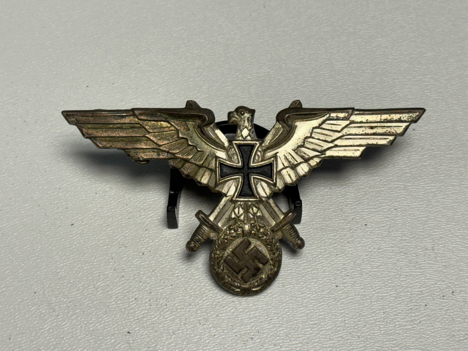 WWII German Wehrmacht Veteran’s Eagle Badge with Iron Cross & Crossed Swords: WWII German military veteran’s association badge featuring a dramatic spread-winged eagle composition centered by a black enameled Iron Cross, with crossed swords extending below and a suspended wre