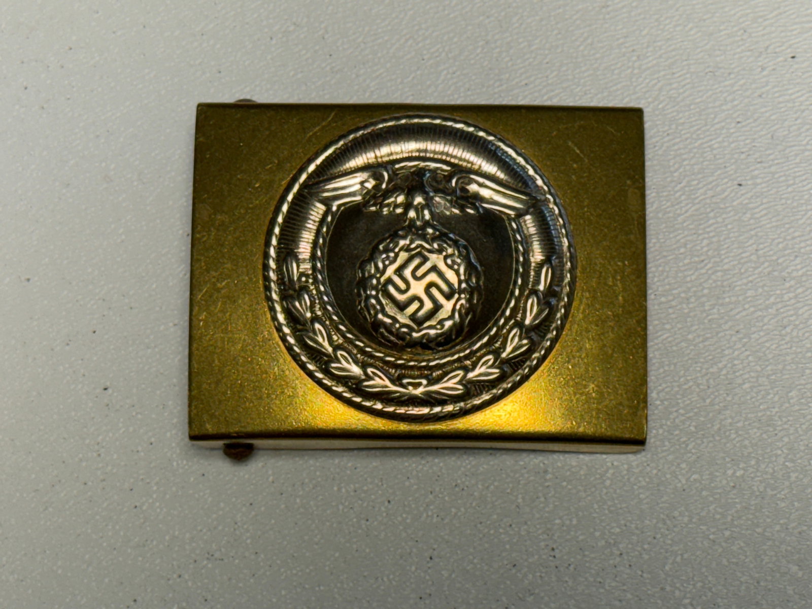 WWII German Political Leader Officer’s Dress Belt Buckle with Eagle & Swastika: WWII German political organization dress belt buckle featuring a rectangular gold-tone body fitted with an elaborate silver-tone circular central device. The centerpiece displays a national eagle clut