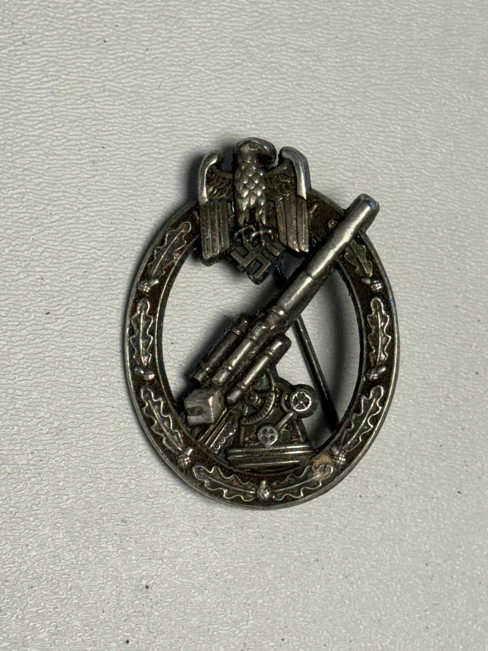 WWII German Army Heer Anti-Aircraft Flak Artillery Badge – Wien Marked: WWII German Army Heer anti-aircraft artillery badge featuring a detailed 88mm-style Flak gun positioned within an oval oak-leaf wreath and surmounted by the German Army eagle and swastika. The dimensi