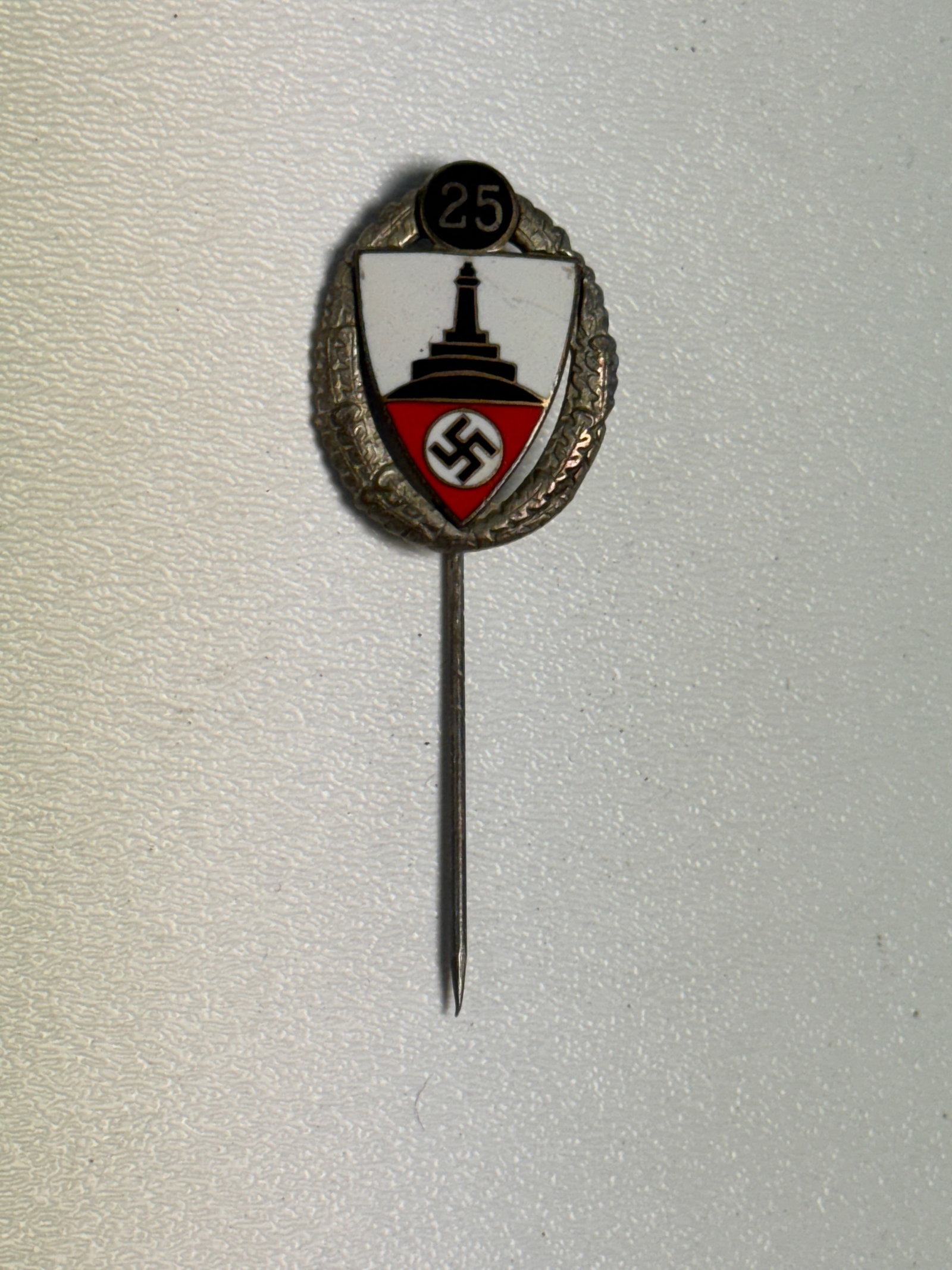 WWII German NSDAP 25-Year Service Honor Pin Enameled Long Service Badge: WWII German long service stickpin featuring an oval silver-tone wreath surrounding a colorful enameled shield, with a prominent black “25” medallion positioned above. The central shield displa