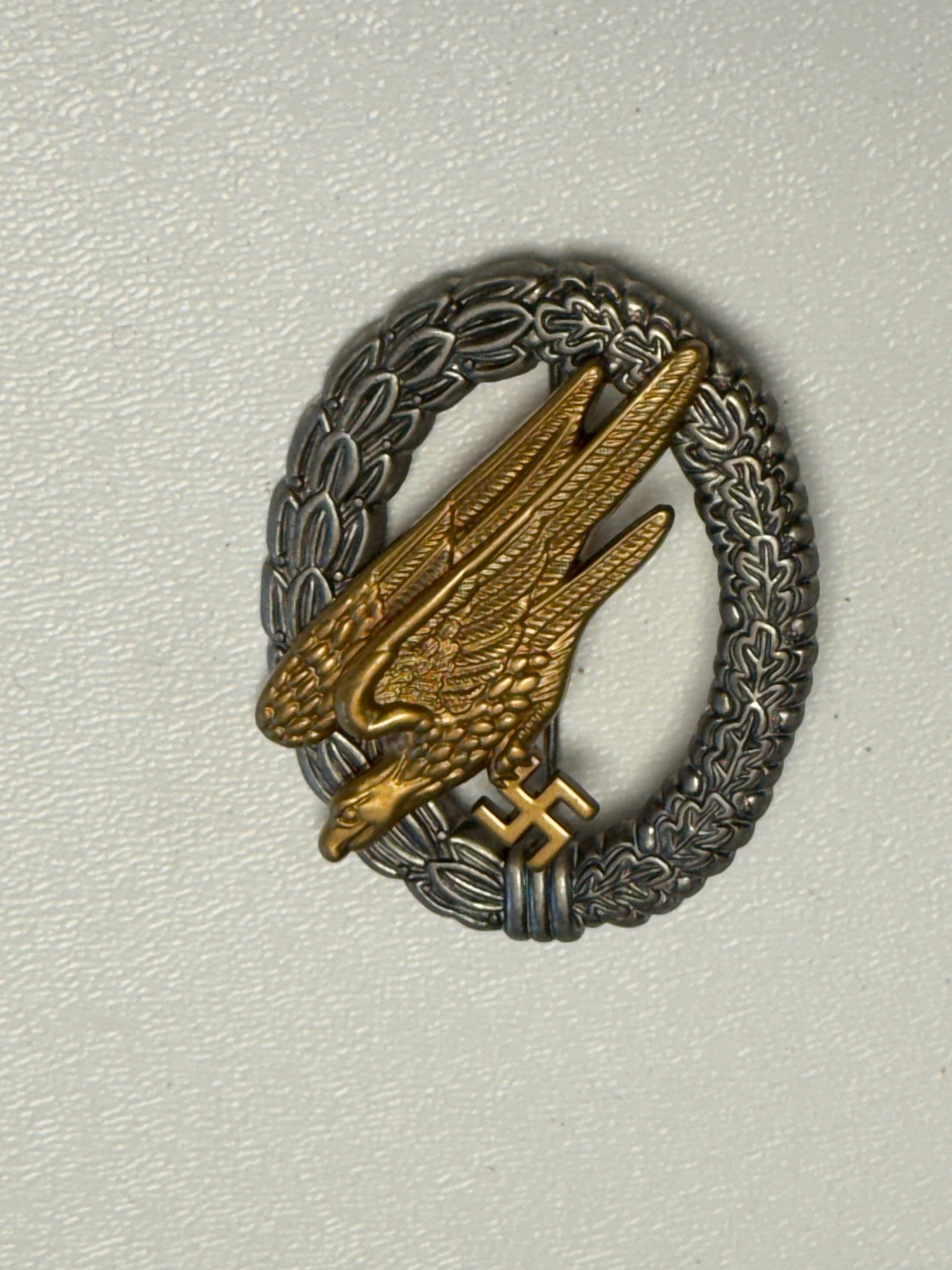 WWII German Luftwaffe Paratrooper Fallschirmjäger Badge: WWII German Luftwaffe Fallschirmjäger paratrooper qualification badge featuring the distinctive diving eagle with outstretched wings clutching a swastika, set within an oval wreath composed of laurel