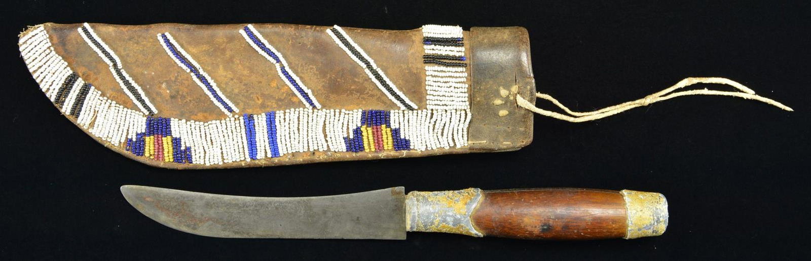 FINE PLAINS INDIAN DOUBLE SIDE BEADED & TACKED: KNIFE SHEATH & KNIFE. 10” x 2.75”, sinew sewn on bridle leather, rarely seen combination of both bead & tack decoration on sheath. ¾” black and white beaded decoration around ci