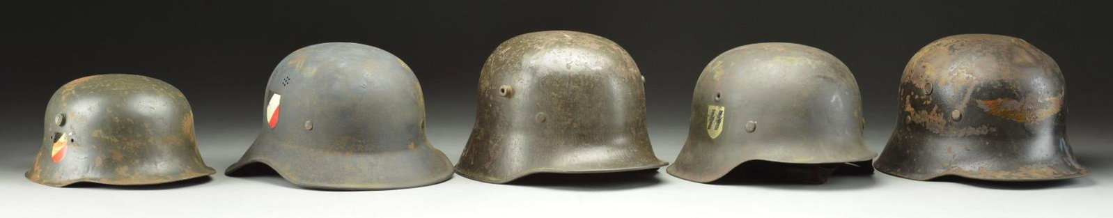 5 WWI & WWII AXIS HELMETS.: 1) AUSTRIAN. A WWII reissued Austrian screened vent helmet. Helmet has a black painted finish with a Luftschutz decal on the front. There is no liner or chinstrap but a partial band is present. CONDIT