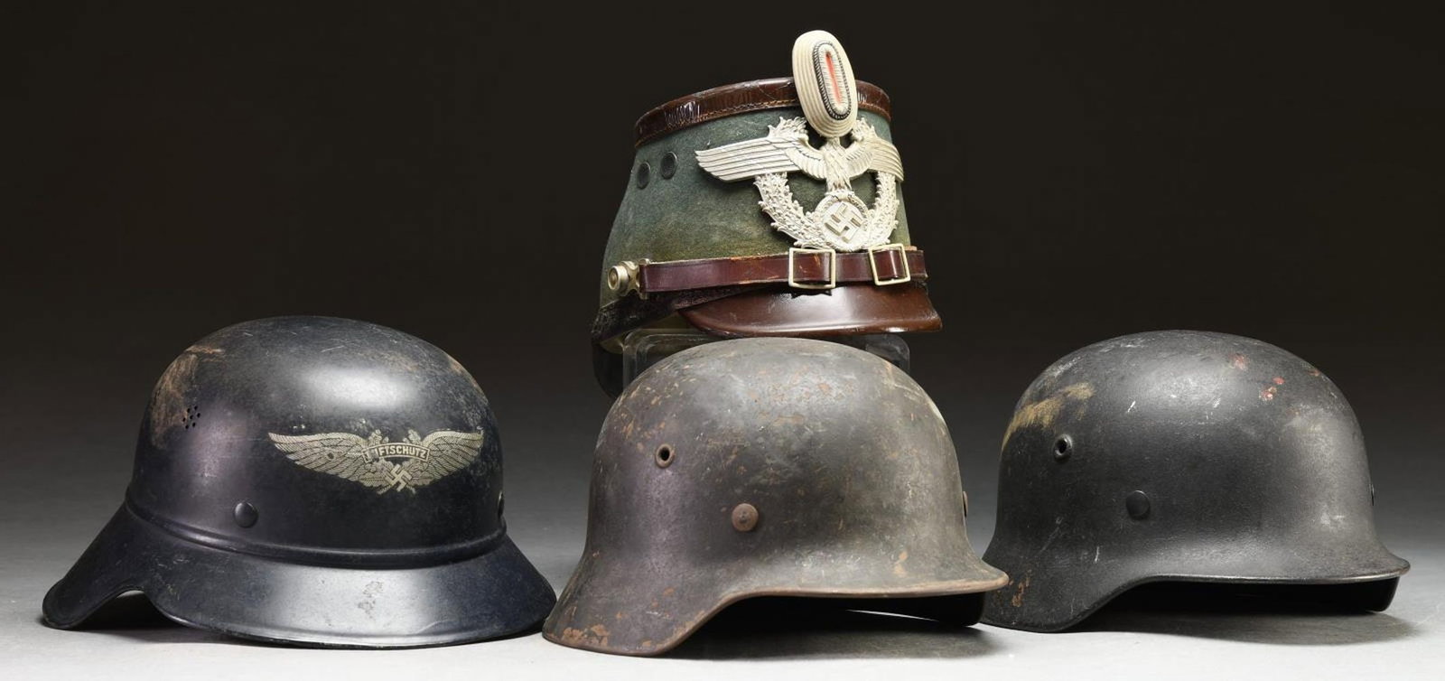 4 WWII GERMAN HELMETS.: 1) KRIEGSMARINE. An M1940 Kriegsmarine helmet with a single gold Wehrmacht eagle on the left side. The body of the helmet is painted dark gray/green. The interior left of the helmet is stamped "ET62",