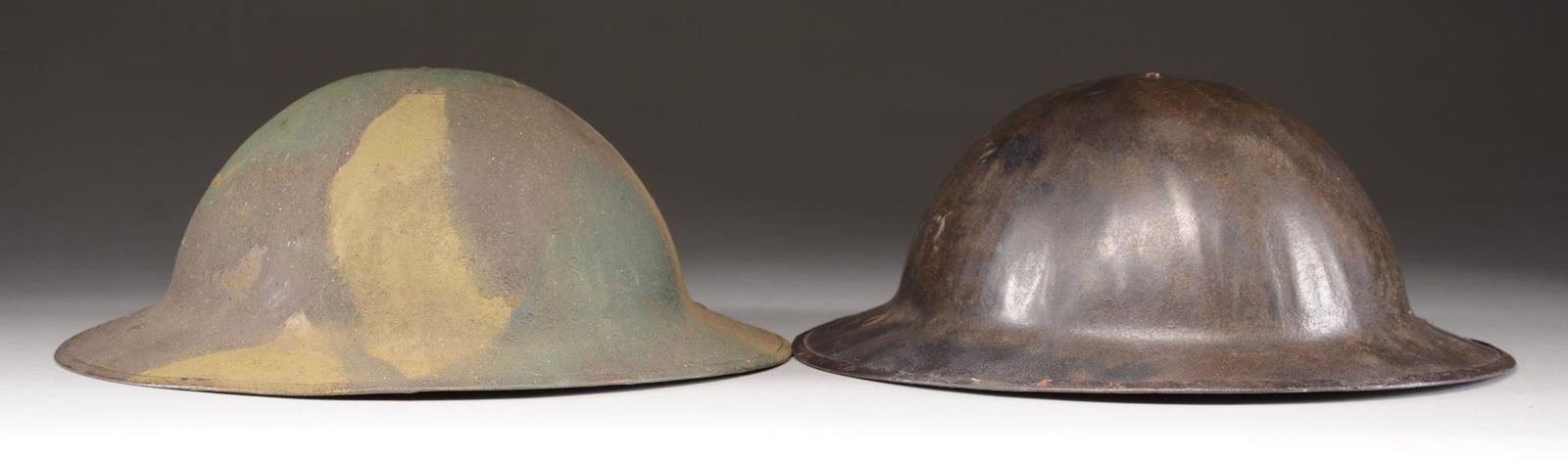 2 US M1917 HELMETS.: 1) CAMOUFLAGE. A lightly camouflaged painted helmet from the WWI period. The heavily sanded finish is light green, dark green, and olive green. Black leather liner with padded crown. No chinstrap. CON