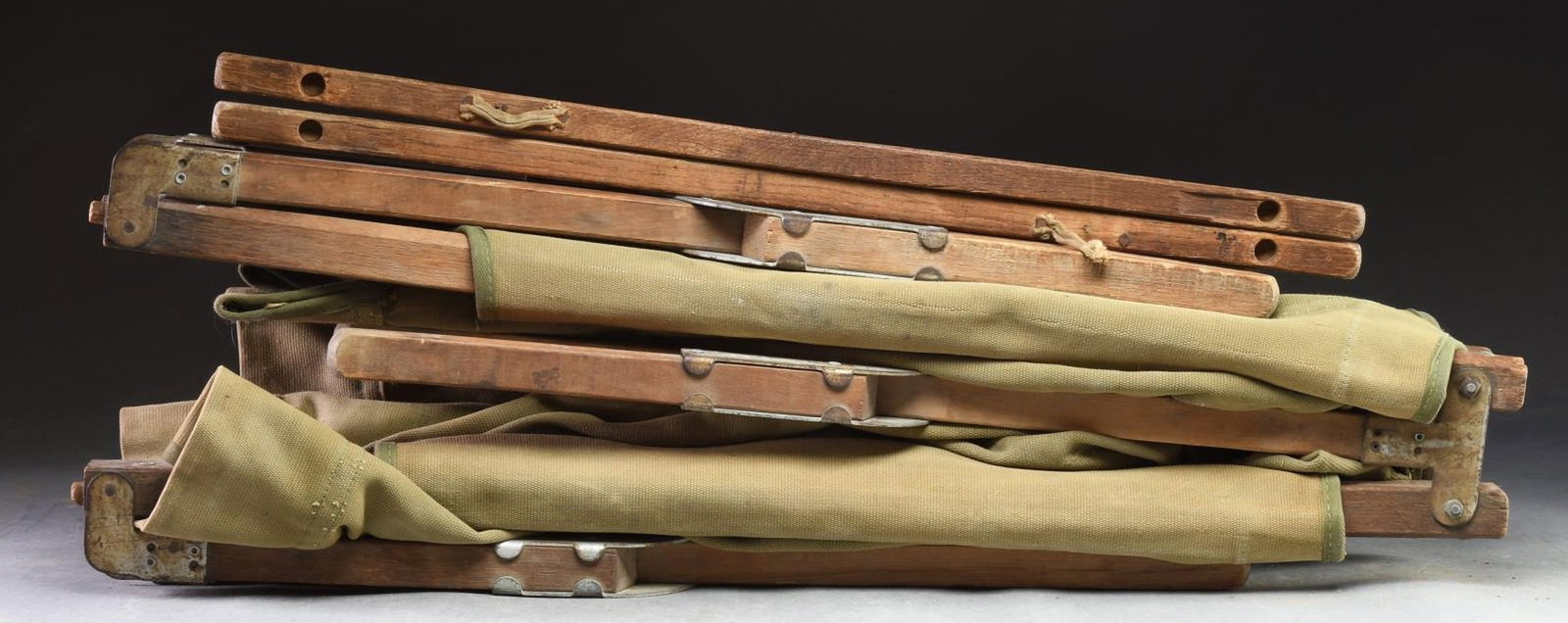 COLLAPSIBLE ARMY CAMPING COT.: Folds out to measures approx. 7' x 2 1/4' x 1 1/2'. OD green canvas covering w/ 2 stabilizing posts. CONDITION: fair showing holes, stains, & oxidation. (02-19681/MD). $20-40.