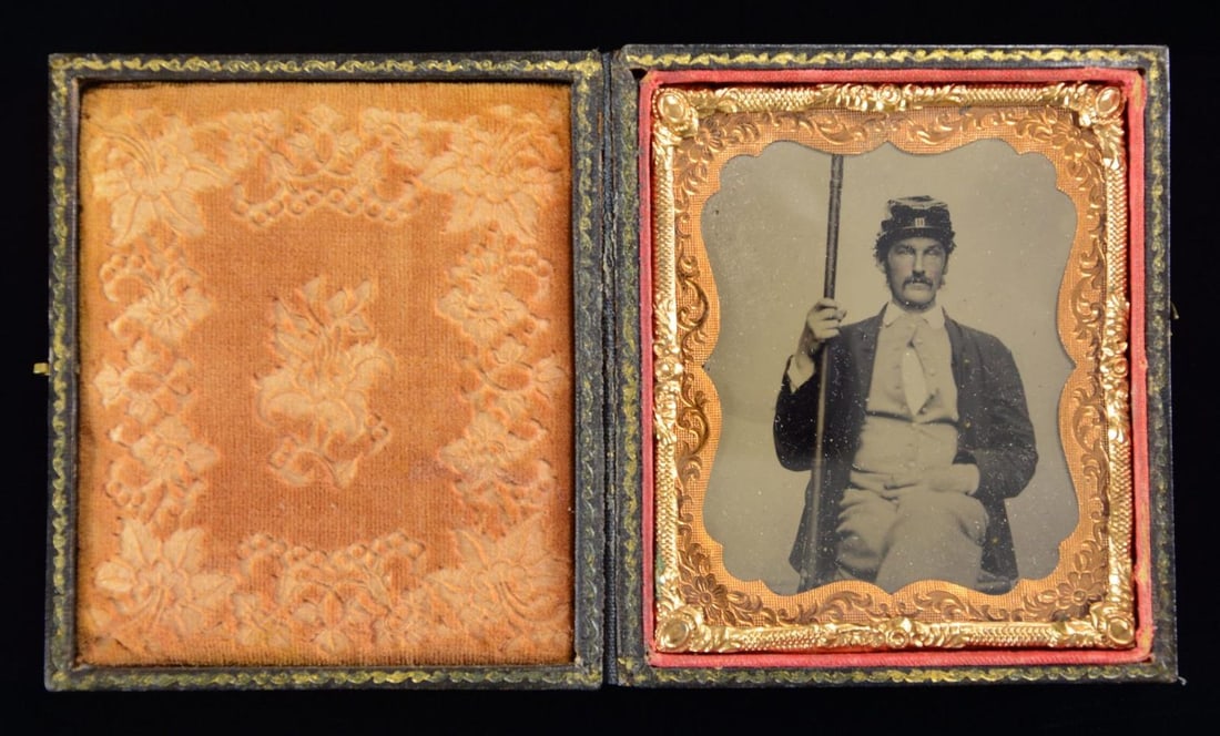 CIVIL WAR TINTYPE OF AN INFANTRY SOLDIER.: This 6th plate tintype depicts a knees-up view of a seated Infantry Private. He wears sky blue pants & vest with a 4-button sack coat over it. In his right hand is a musket. On his head is an interest