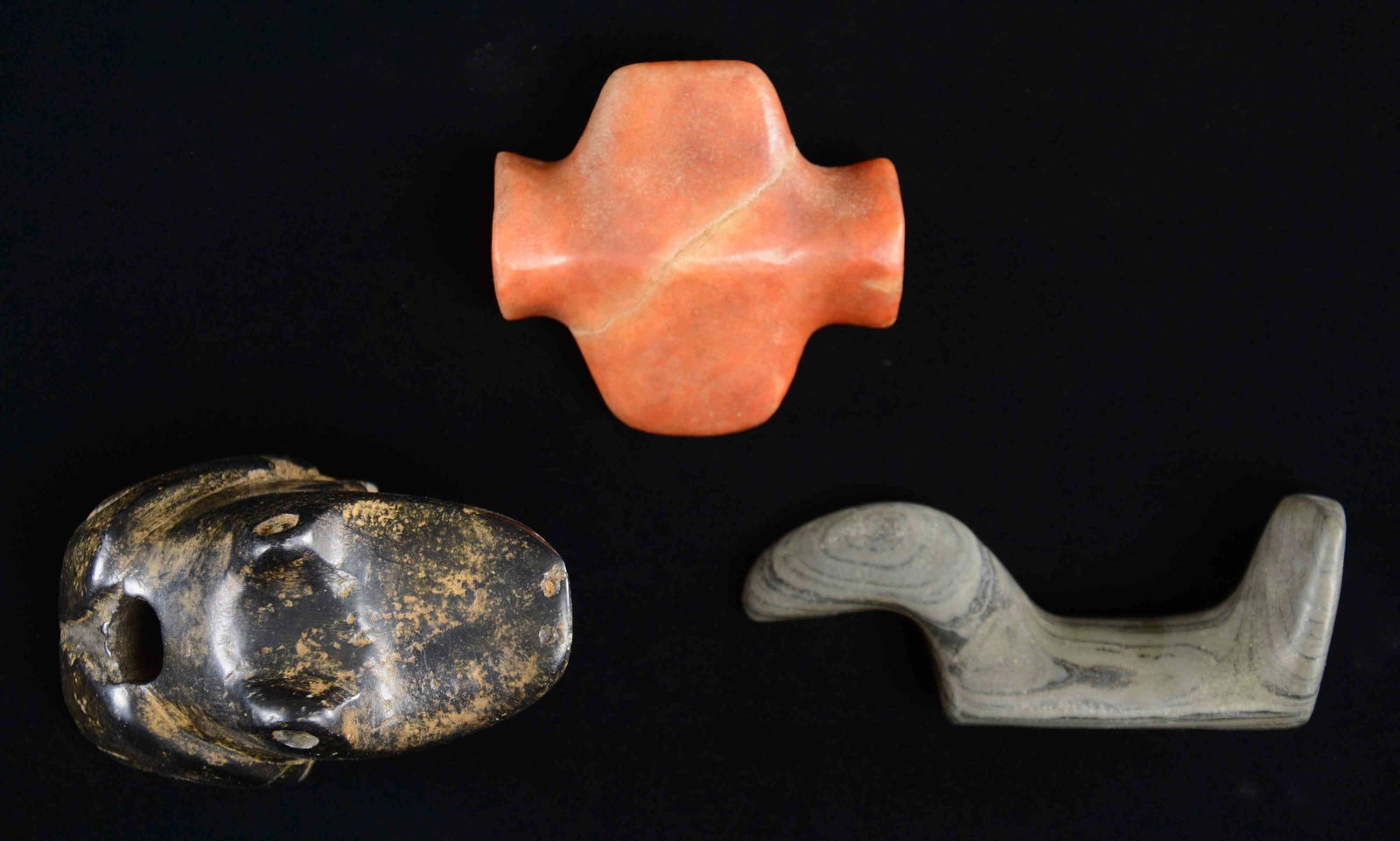 THREE ARCHAIC STYLE NATIVE AMERICAN CARVED STONE: EFFIGIES. 3 polished stone artifacts; each 3-4", one is black stone in the shape of a frog with large tapered hole drilled through back. Gray striated stone with two holes drilled for string, collecti