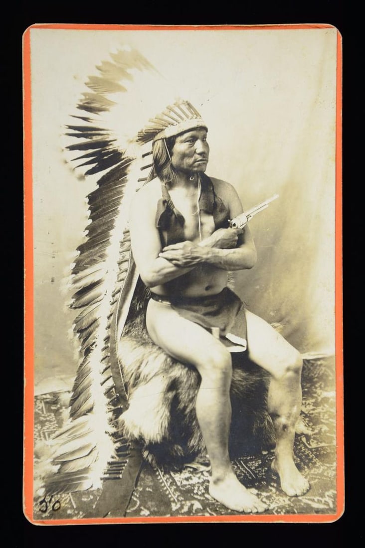 CABINET CARD OF SIOUX CHIEF "PAINTED HORSE" WITH: COLT SAA. Baker & Johnston, Evanston, WY mount, Chief Painting Horse seated on fur covered chair wearing loin cloth & full headdress. Several images of Chief Painted Horse later in life circa 1900 can