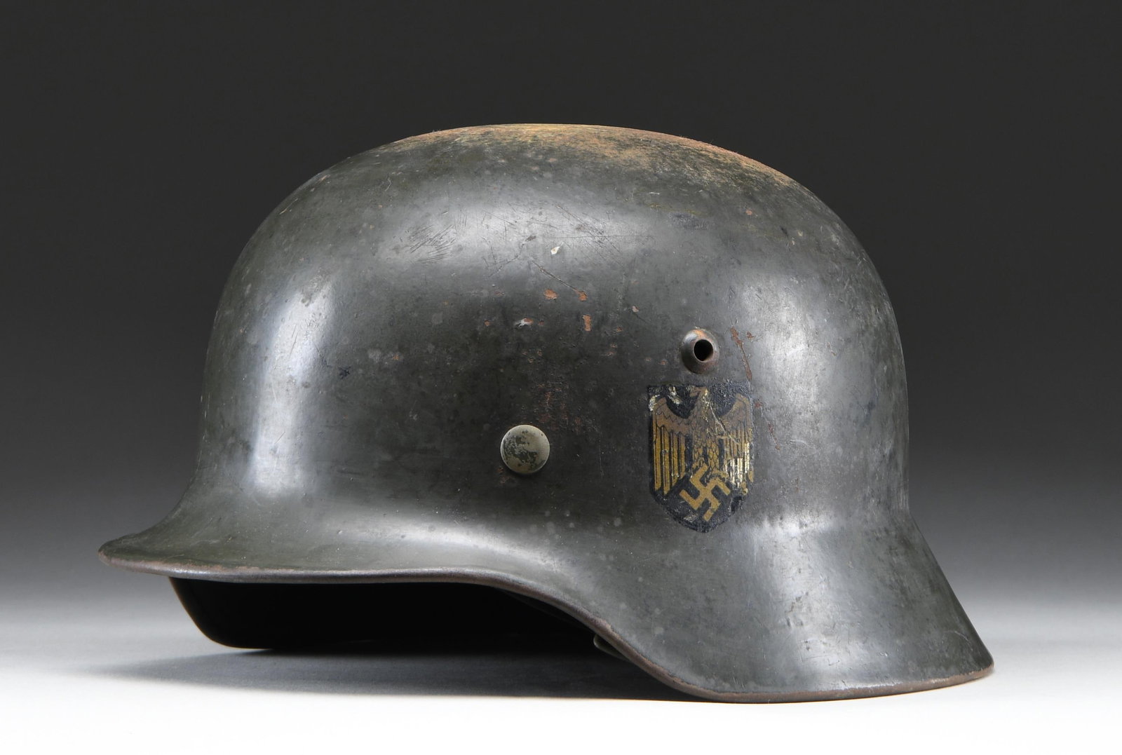 WWII GERMAN M1935 COAST ARTILLERY HELMET.: This helmet has a very dark green-painted finish and has a single Wehrmacht eagle decal on the left side. The decal is distinctly gold in color, and a small scraped area on the eagle's left wing shows