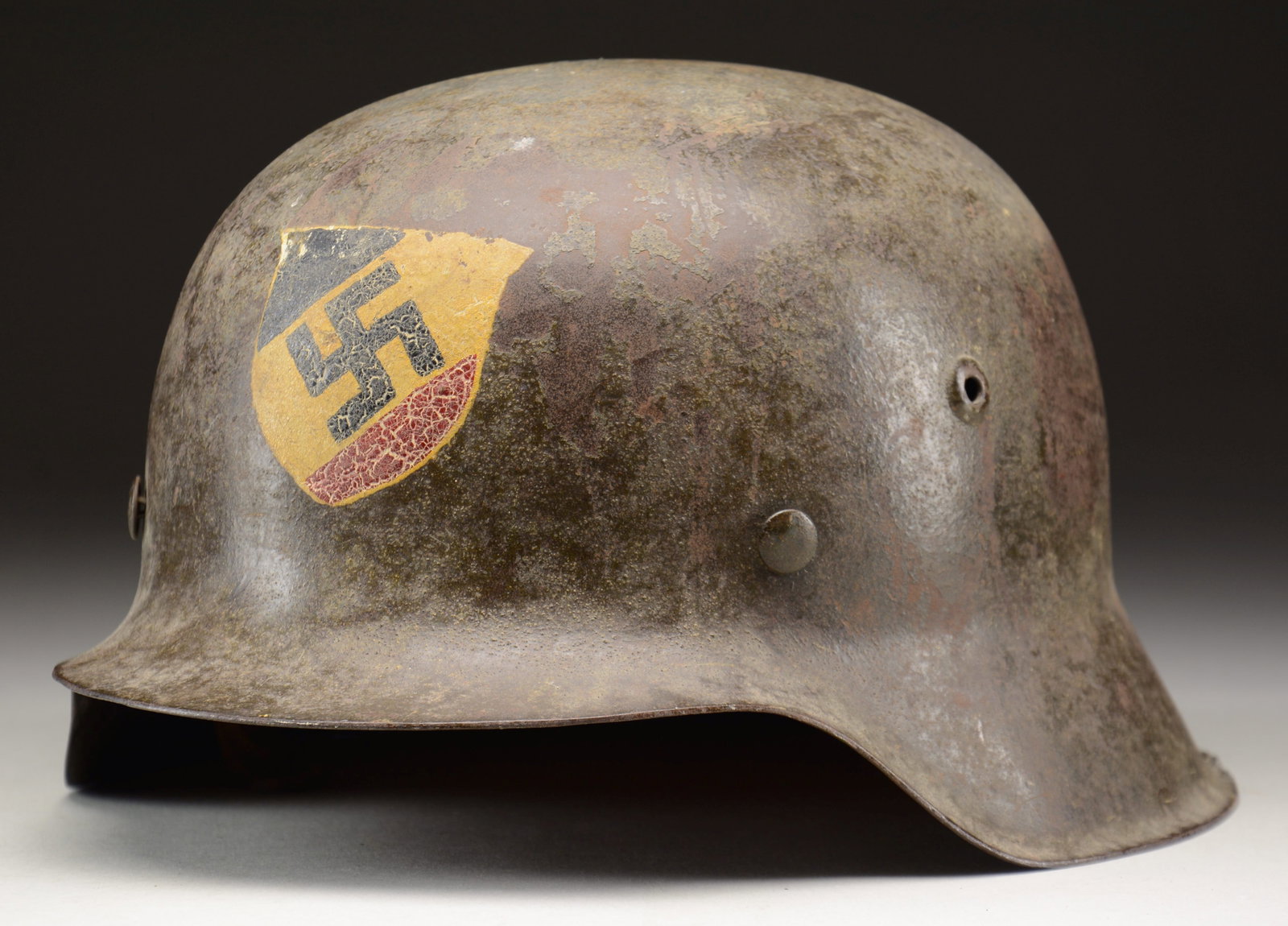 WWII GERMAN M1942 HELMET LIKELY FOR A VOLKSSTRUM: UNIT. A rare and desirable variation of the German M1942 helmet with a dark field green-painted finish and an original white shield painted on the front with a central party symbol in black sandwiched