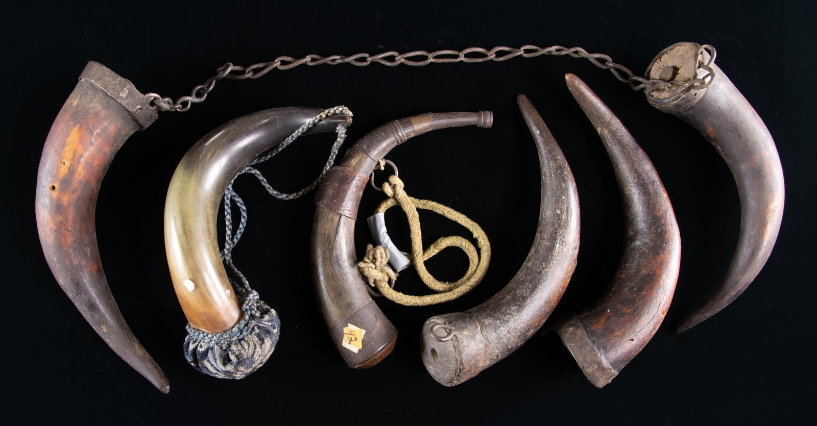 GROUP OF 6 VINTAGE IRON MOUNTED HORNS.: 12" iron mounted powder horn, 2 large iron carrying rings. Four 12" iron mounted dark storage horns; 12" decorative green horn with 6 brass hooks and cushioned top, blue cord. CONDITION: good overall,