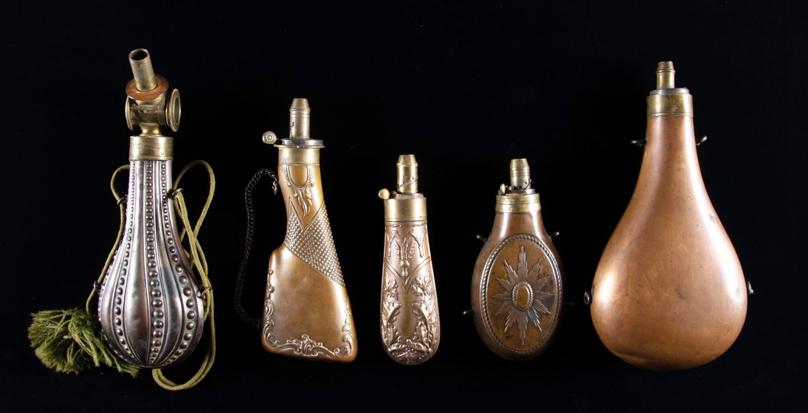 FIVE UNUSUAL POWDER FLASKS.: 10" flask with patent charger with glass windows and rotating top, 9" gun stock, 10.5" massive bulbous, oblong & oval flasks. CONDITION: good to very good overall. PROVENANCE: The Esteemed Norm Greenb