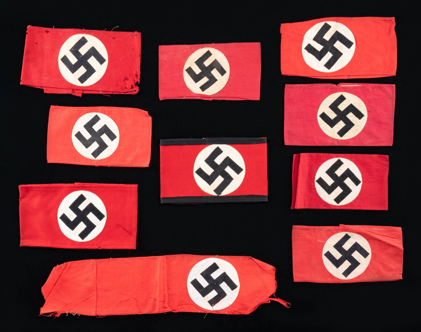 WWII GERMAN SS AND PARTY ARMBANDS: This nice lot of WWII German armbands includes 1 SS armband with a sewn black grosgrain party symbol on a white grosgrain disk, all on a red wool field with black borders. / 1 Party armband with an em