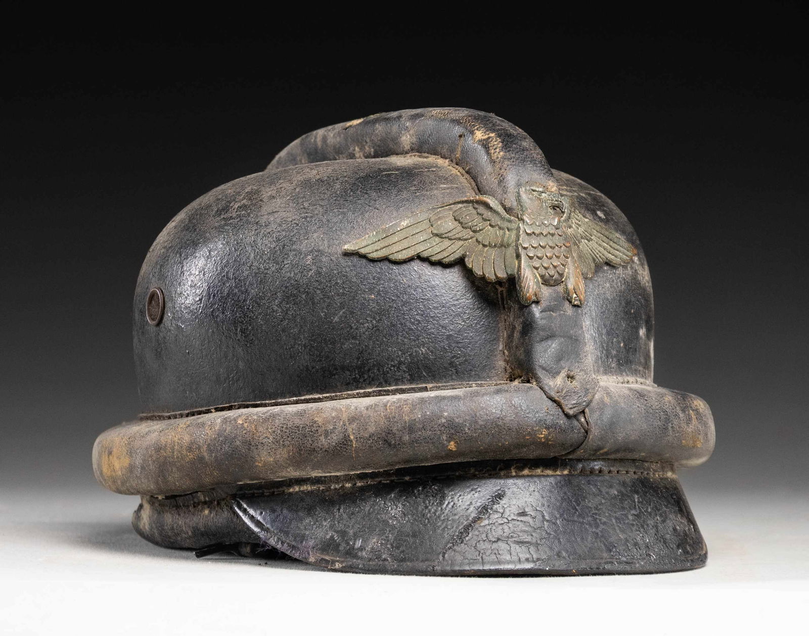 WWII GERMAN NSKK 1ST PATTERN MOTORCYCLE HELMET.: A good representative example of a 1st model WWII German NSKK helmet in black leather. The helmet is complete with ear flaps and the neck flap. The eagle front plate is missing the bottom half that co