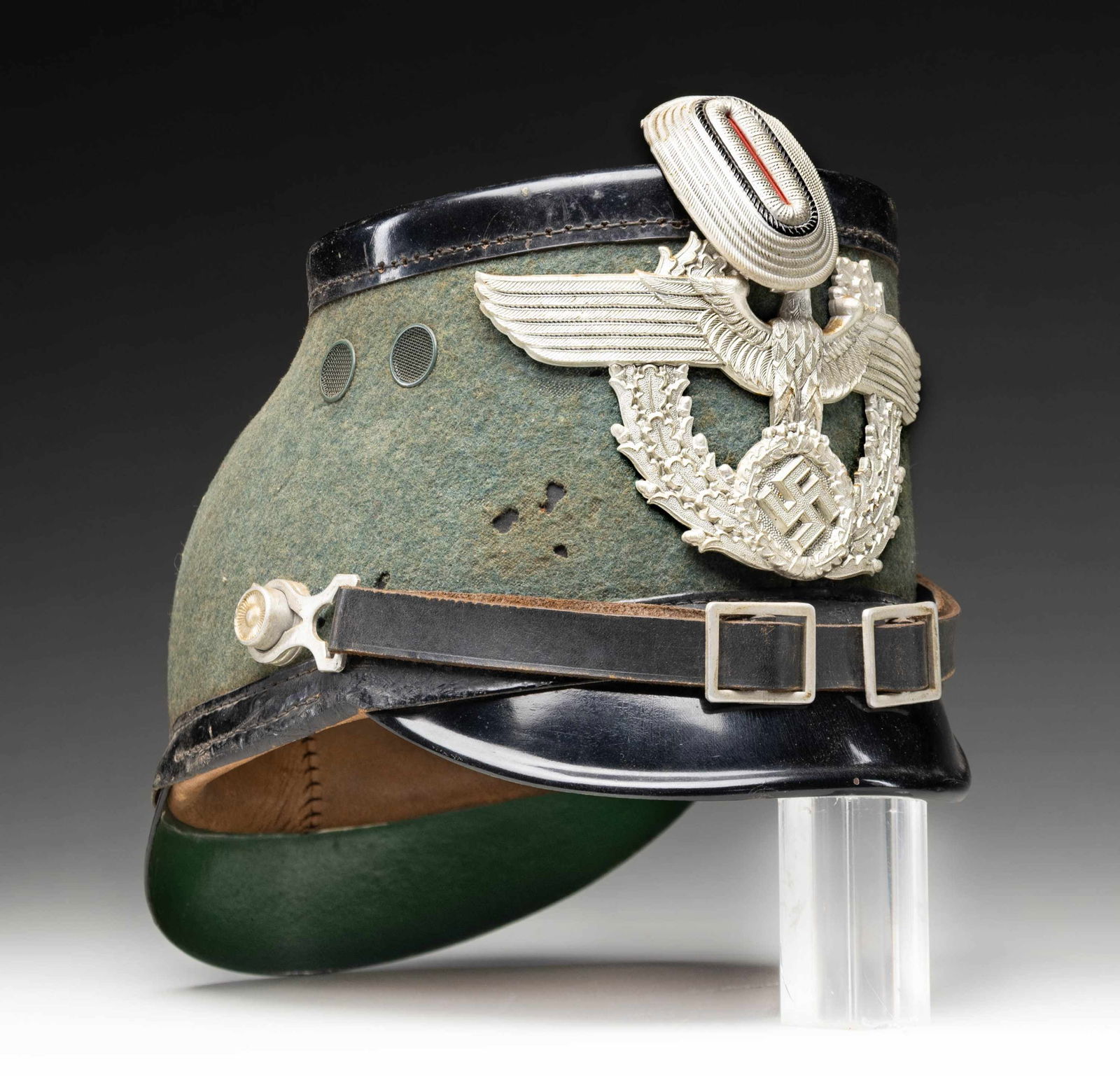 WWII GERMAN POLICE SHAKO.: This well worn WWII German Police shako has a green felt body with a black leather trim. Large Police eagle front plate and metal cockade at the top of the front. Complete chinstrap. 8 tongue brown le