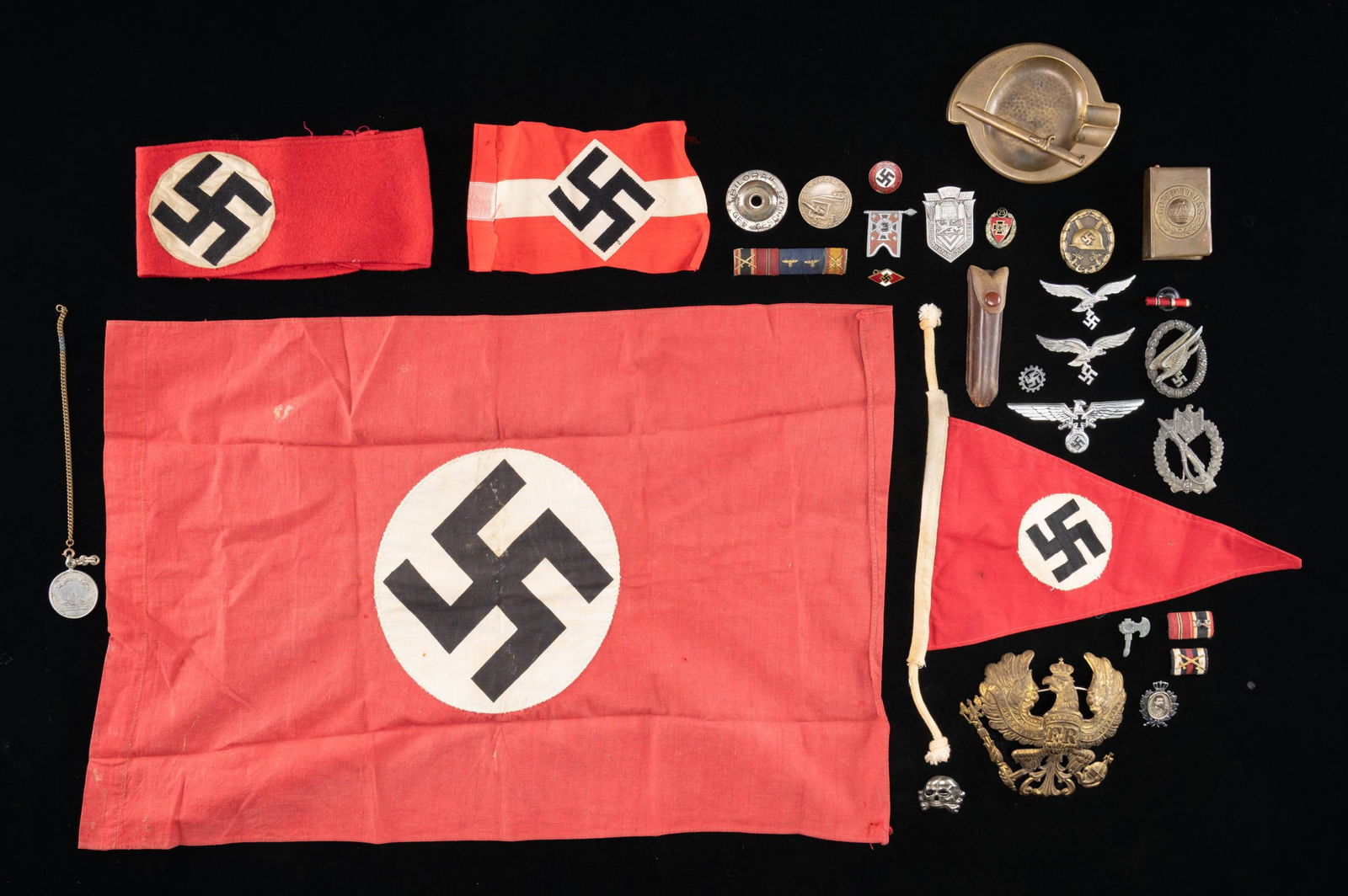 LARGE AND VARIED WWII GERMAN MILITARIA GROUP.: This extensive lot includes 1 Party pennant, 1 HJ armband, 1 wool Party armband, 1 small Party flag, 1 WWI Prussian spike helmet eagle in gilded brass, 1 WWI match safe, 1 brass WWI ashtray with bayon