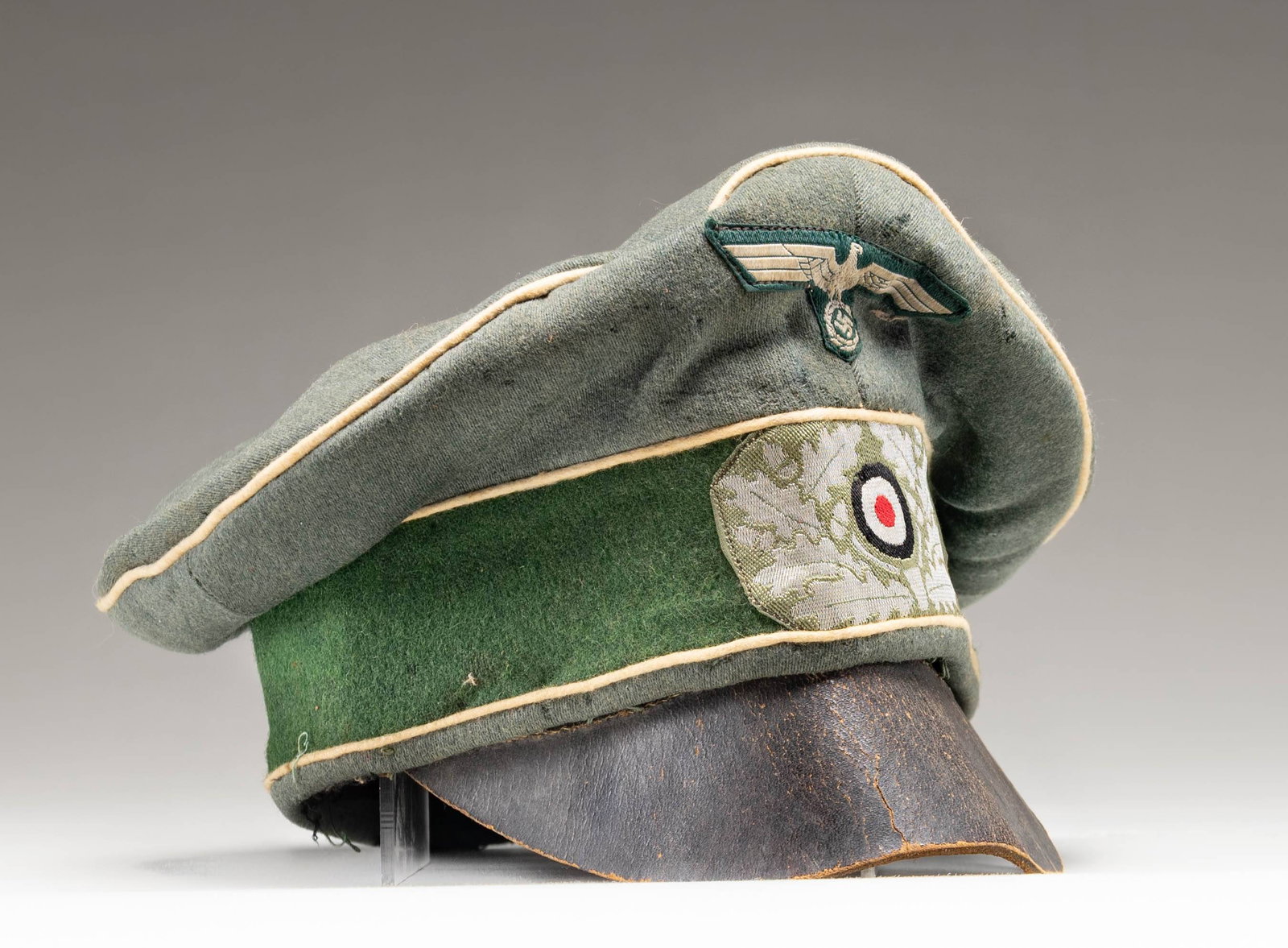 EARLY WWII GERMAN OLD STYLE OFFICERS FIELD CAP.: A good example of a scarcer early WWII officer's field cap in sage green with white piping for infantry. This is a crusher type cap with no real form and a rough heavy leather visor. There is a sewn c