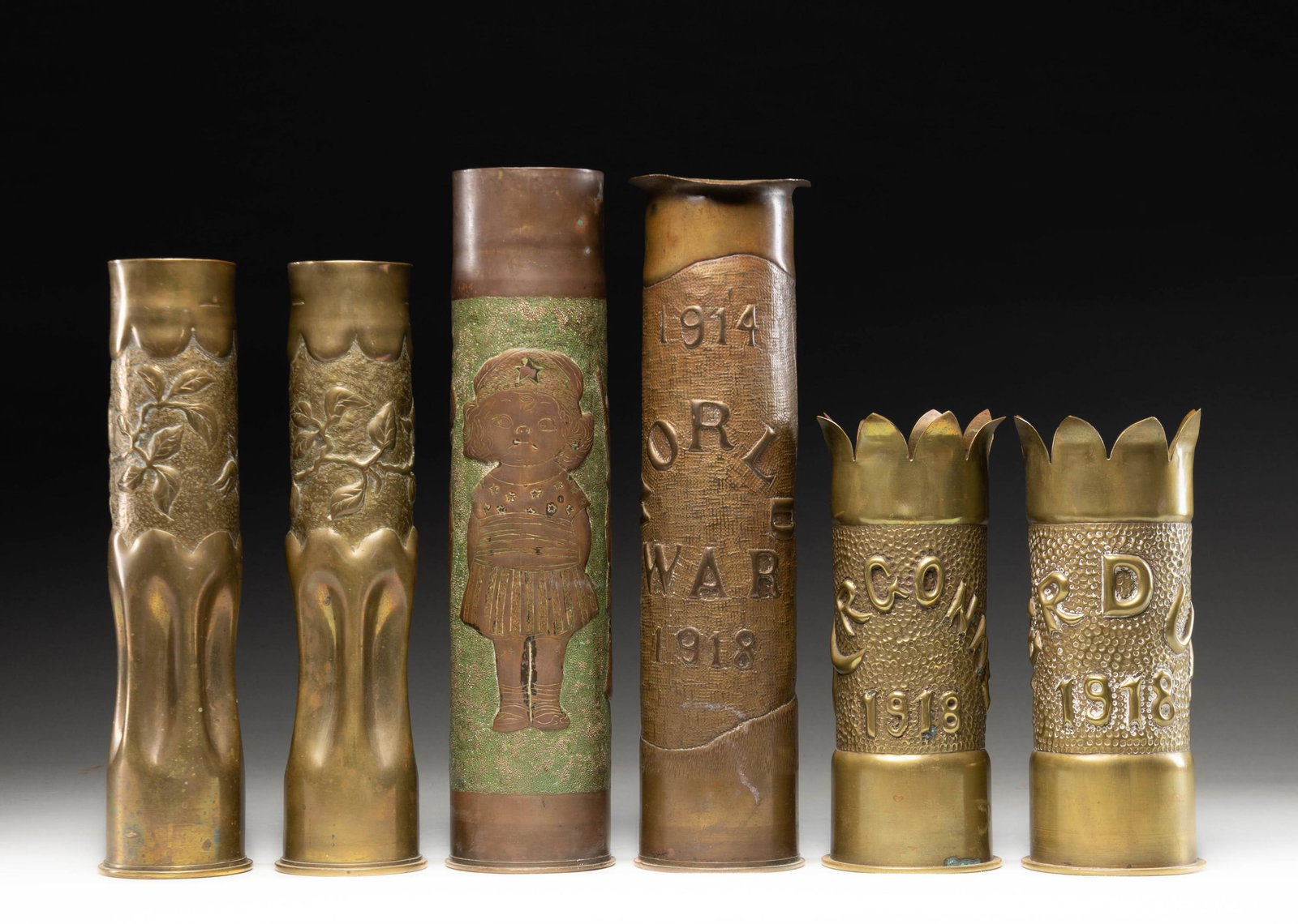 SIX WW1 TRENCH ART SHELLS.: Souvenir shell casings made into vases, 75mm and others, folk art-repousse design, "ARGONNE 1918", VERDUN 1918". CONDITION: very good overall. PROVENANCE: estate collection of Compton Labauve. (02-264