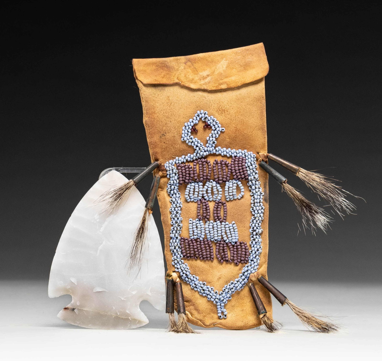 SMALL NATIVE AMERICAN STYLE BEADED TOBACCO POUCH &: SPEAR POINT. 7" x 4" leather pouch with beaded design and tinkle bell decoration, 3" x 4" chipped translucent stone spear point. CONDITION: good. (02-25745/JS). NON-GUN. $200-300.