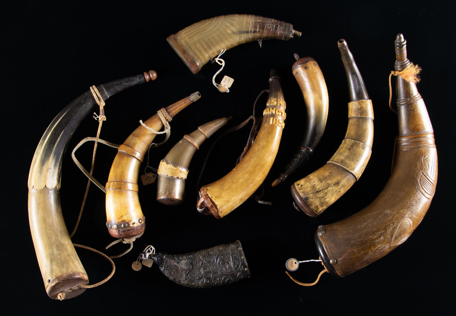 GROUP OF 9 RAISED RELIEF CARVED POWDER HORNS.: Variety of shapes and sizes, all have raised carved relief design, mostly 19th century, 7" to 15", one named 10" "J SMITH / HANGTOWN / 1850", old collection tags. CONDITION: good overall. PROVENANCE: