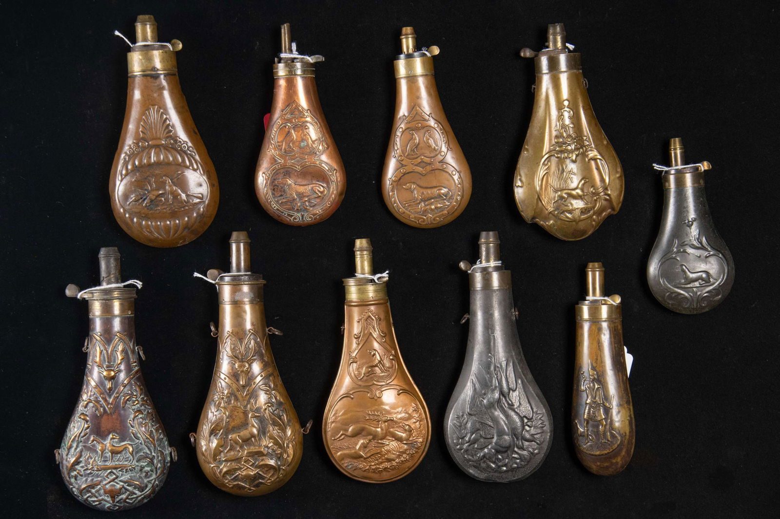 TEN DECORATED HUNTING POWDER FLASKS.: 1) 8" deer and deer head, Riling 988. 2) 7" dog & game, tagged Riling 600. 3) 8" dogs & deer head, "MATHESSON" Riling 570. 4) 7.75" dogs chasing deer, Riling 984. 5) 7.5" white metal, hanging game,