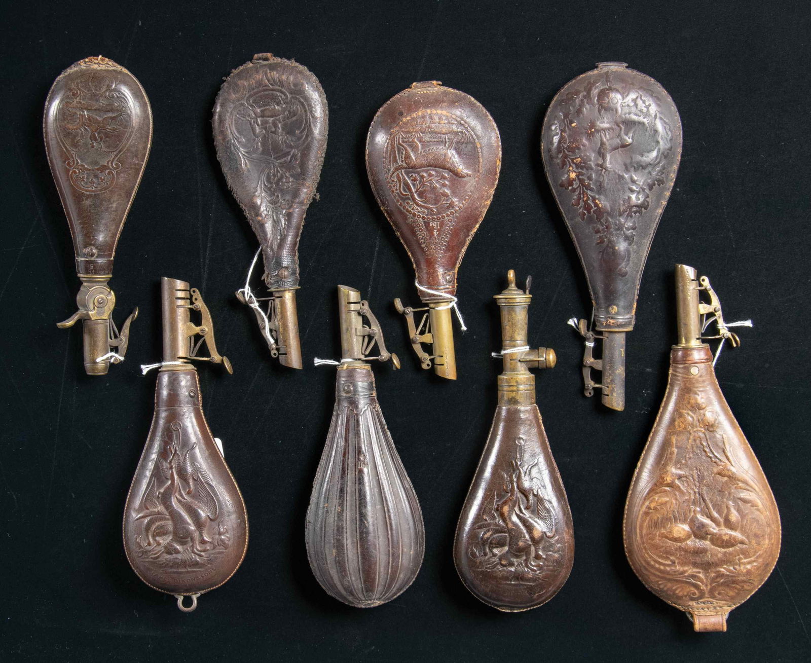 EIGHT VICTORIAN EMBOSSED LEATHER SHOT POUCHES.: Varying 8-9" each with brass measures, 7 are maker marked. CONDITION: good overall, one American Flask company is resewn on edges, the single 4lb unmarked one has hole. (02-25917/JS). NON-GUN. $300-50