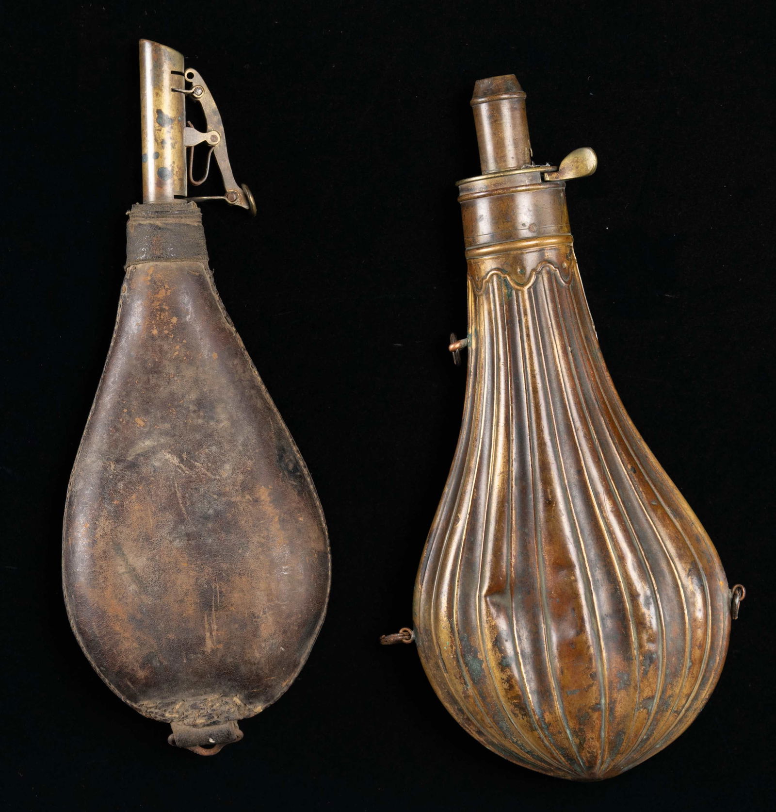 ANTIQUE POWDER & SHOT FLASKS.: 1) AM FLASK & CAP CO. Overall: 10". Copper scalloped body with brass adj. spout. CONDITION: overall has mustard patina appearance with dents & broken spring to lid.2) LEATHER SHOT 6 LB. FLASK. Overall