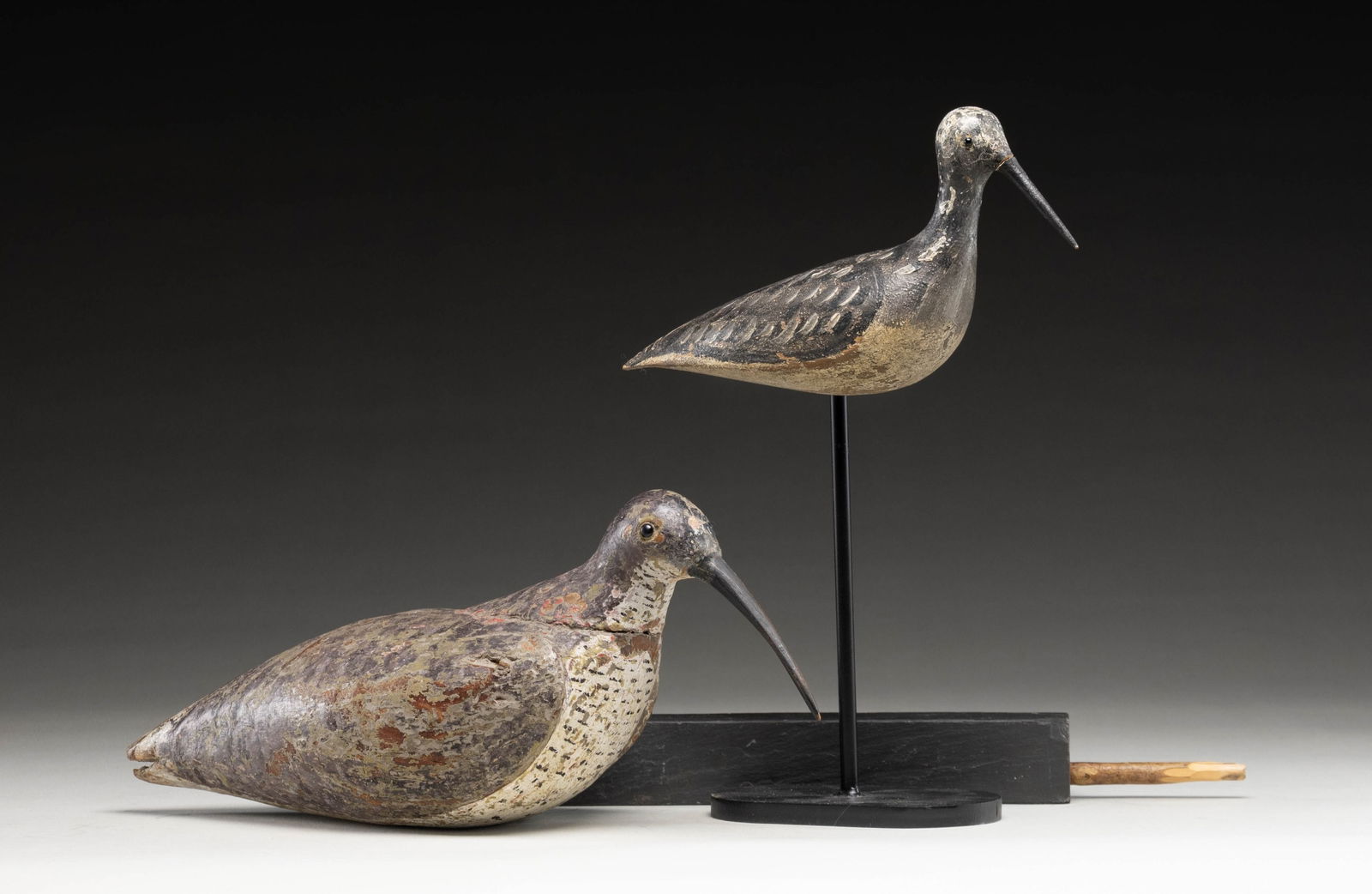 2 SHORE BIRD DECOYS WITH STANDS.: 1) Curlew measures 15" with glass eyes and nicely carved in wings. CONDITION: good; remnants of good old over paint considerably chipped through to wood. Very attractive. With stick and metal stand