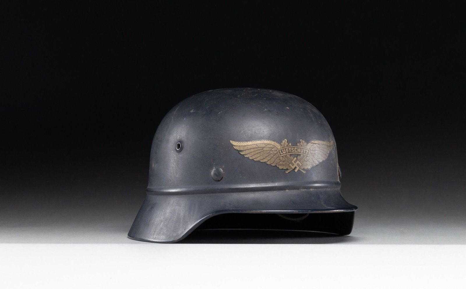SCARCE WWII GERMAN BEADED M35 LUFTSCHUTZ: HELMET. A scarcer example of a WWII German beaded M1935 Luftschutz helmet in dark blue paint with a large winged Luftschutz decal on the front. Inside rear is stamped "2194" and the inside left is