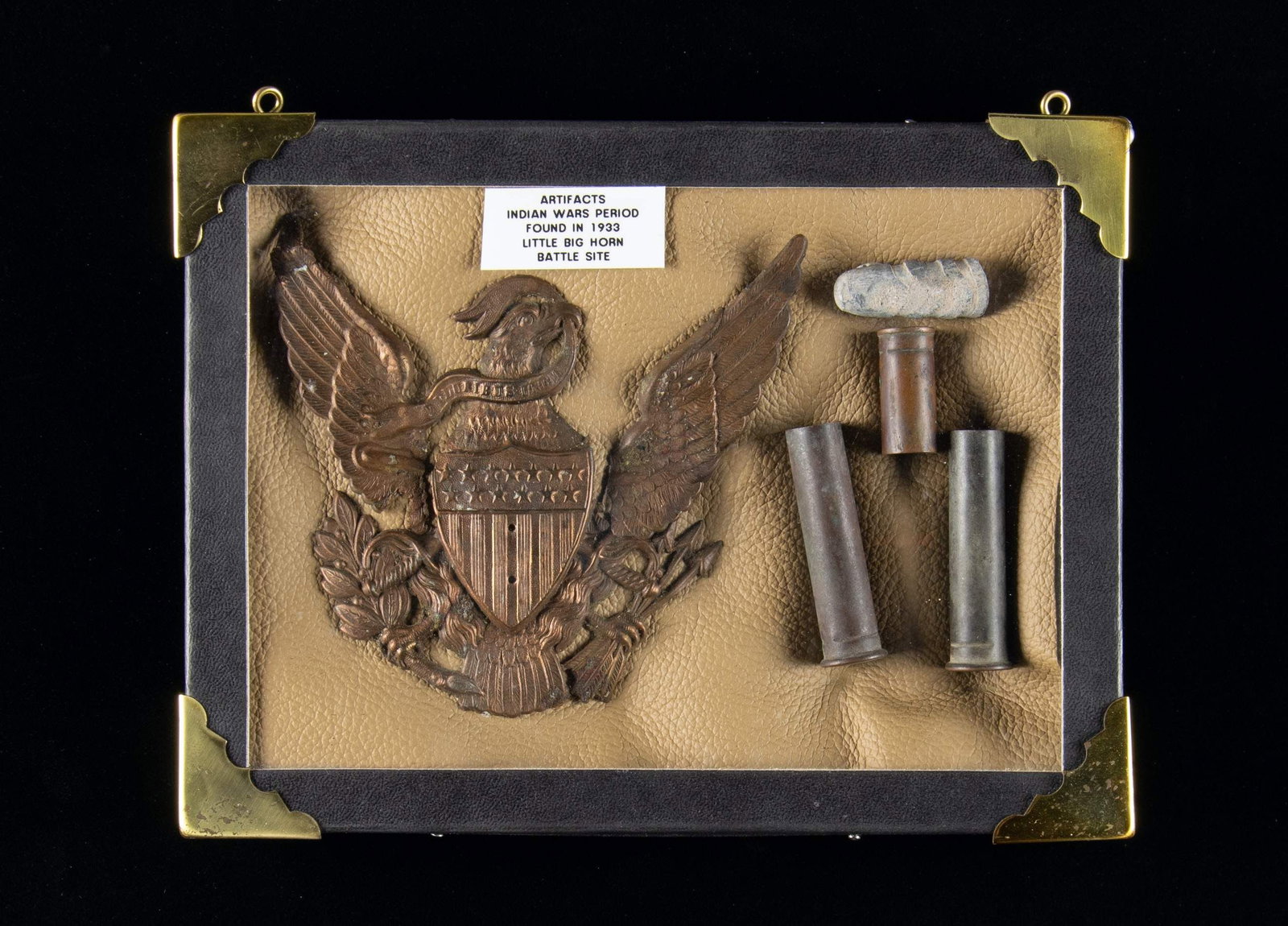 LITTLE BIG HORN EXCAVATED RELICS.: Small Riker box with tag stating the following items were dug up in 1933. Box contains bullet, 3 cartridges cases & US Cavalry insignia. CONDITION: Items shows patina. (02-26592/MD). $150-250.