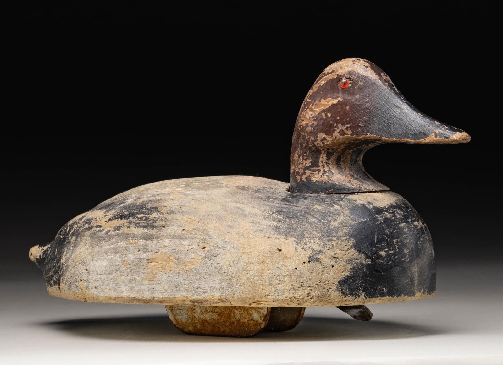 UNMARKED CANVASBACK DRAKE DECOY.: Canvasback drake decoy crafted by an unknown maker. Decoy measures approx. 18" in length, featuring black and brown plumage with red glass eyes. Underside is fitted with a brass screw and leather stra