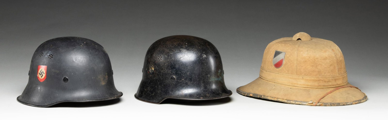 3 WWII GERMAN HELMETS.: 1) WWII German civic curved dip helmet with a black painted finish featuring a Police decal on the left side and a national decal on the right. The inside rear is stamped with a logo inside a