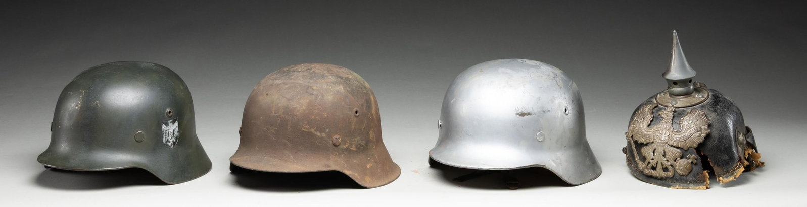 4 WWI & WWII GERMAN HELMETS.: 1) WWII German M1942 battle helmet with a dark gray / green painted finish. No stampings are noted on the interior. Complete original leather liner with a trace of the chinstrap remaining. CONDITION: