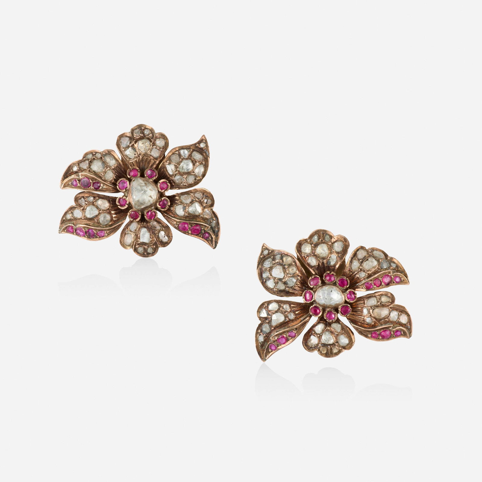 Victorian, Two diamond and ruby dress clips: Victorian Two diamond and ruby dress clips Each of floral design, set with circular-cut rubies and rose-cut diamonds Gilt metal Each 1.125 x 1.375 in; Gross weight 14.7 dwts This work will ship from
